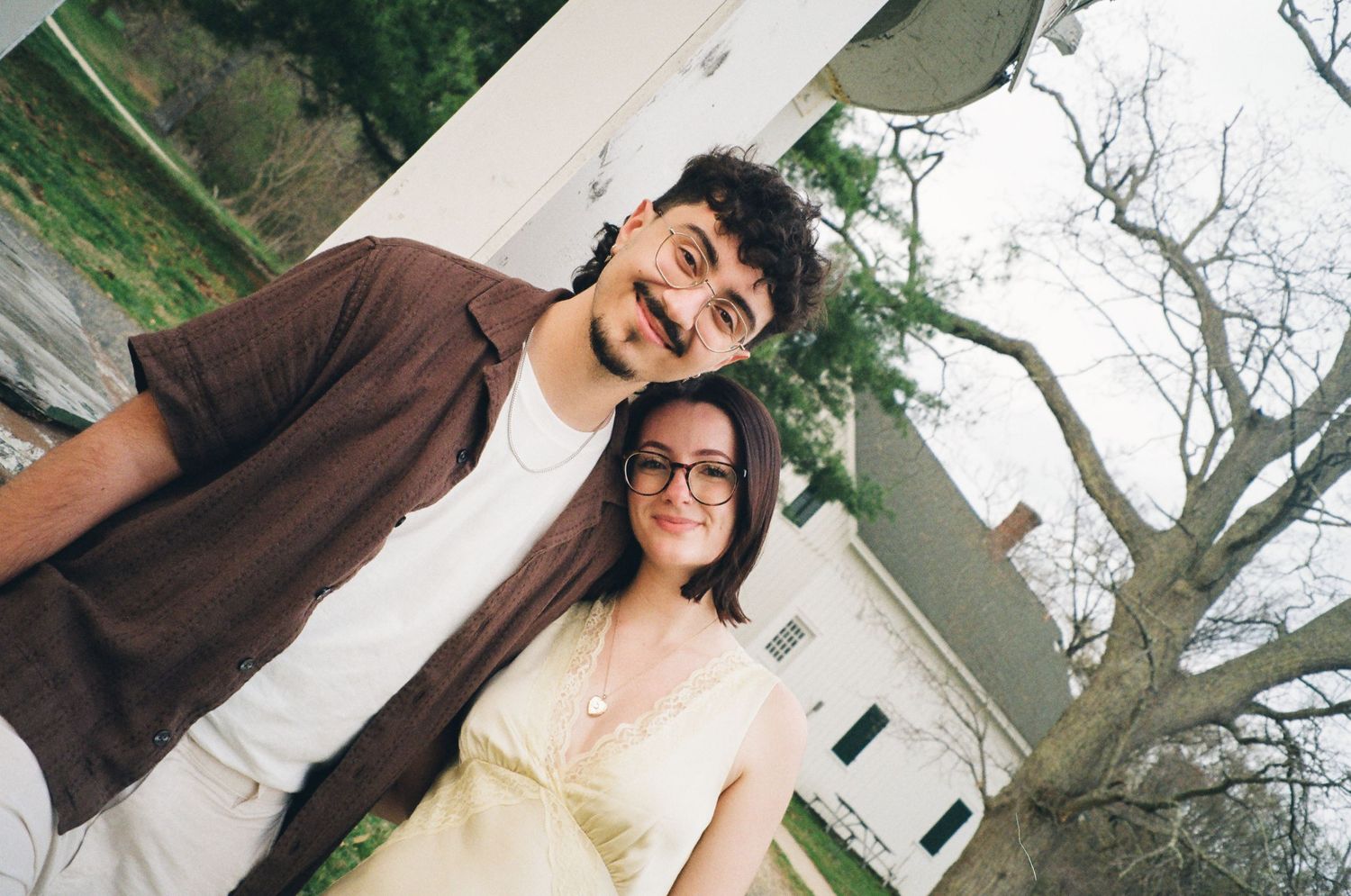 Happy couple taking a low-angle selfie outdoors near a white building with bare trees.