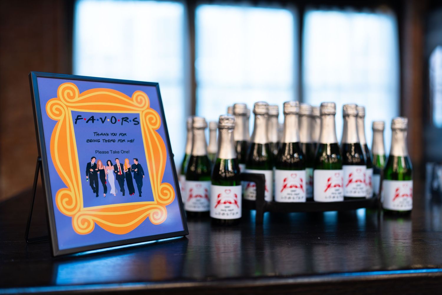 Friends TV show themed party favors table with mini champagne bottles and framed sign.