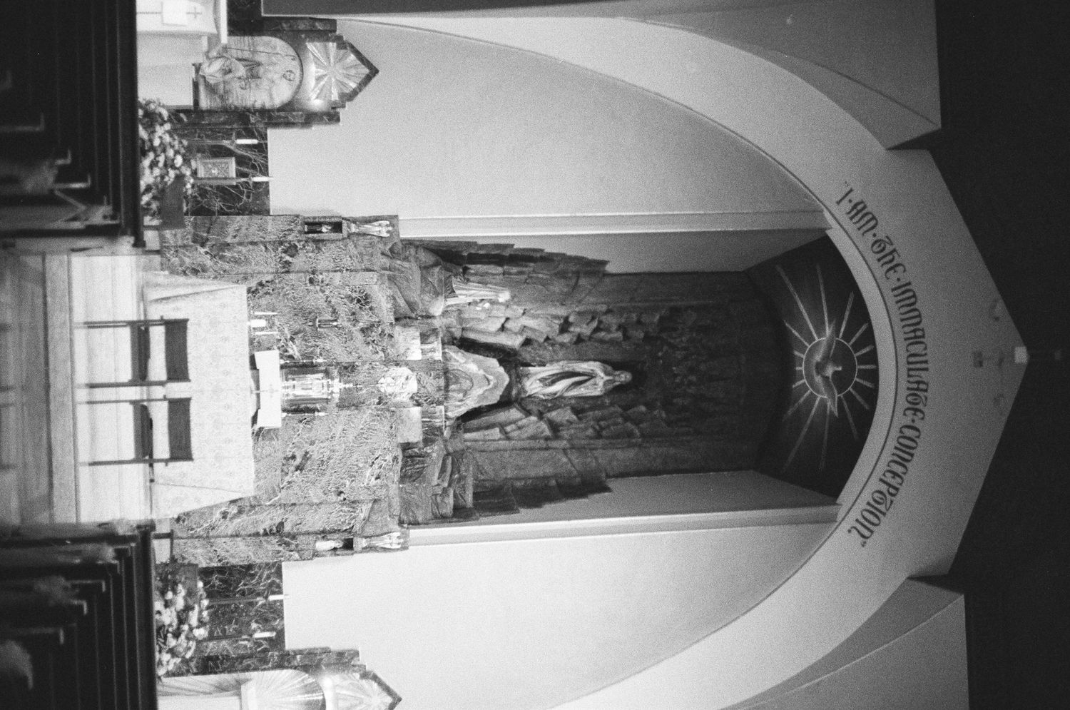 Black and white photo of ornate church interior with arched entrance and decorative stonework.