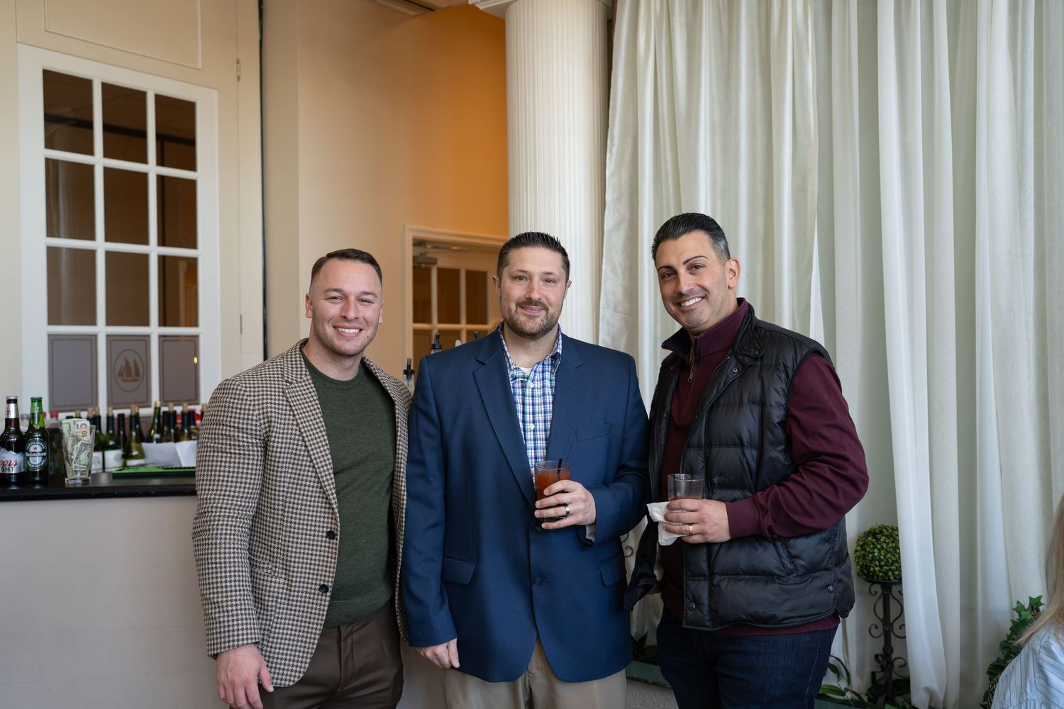 Three men in business casual attire holding drinks at a RE/MAX Edge networking reception.