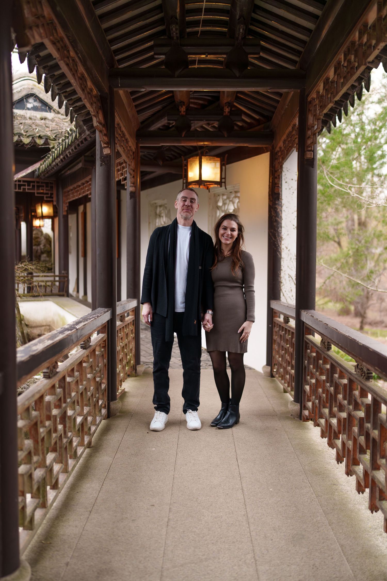 Happy couple standing hand in hand in an elegant traditional Chinese architectural covered corridor.