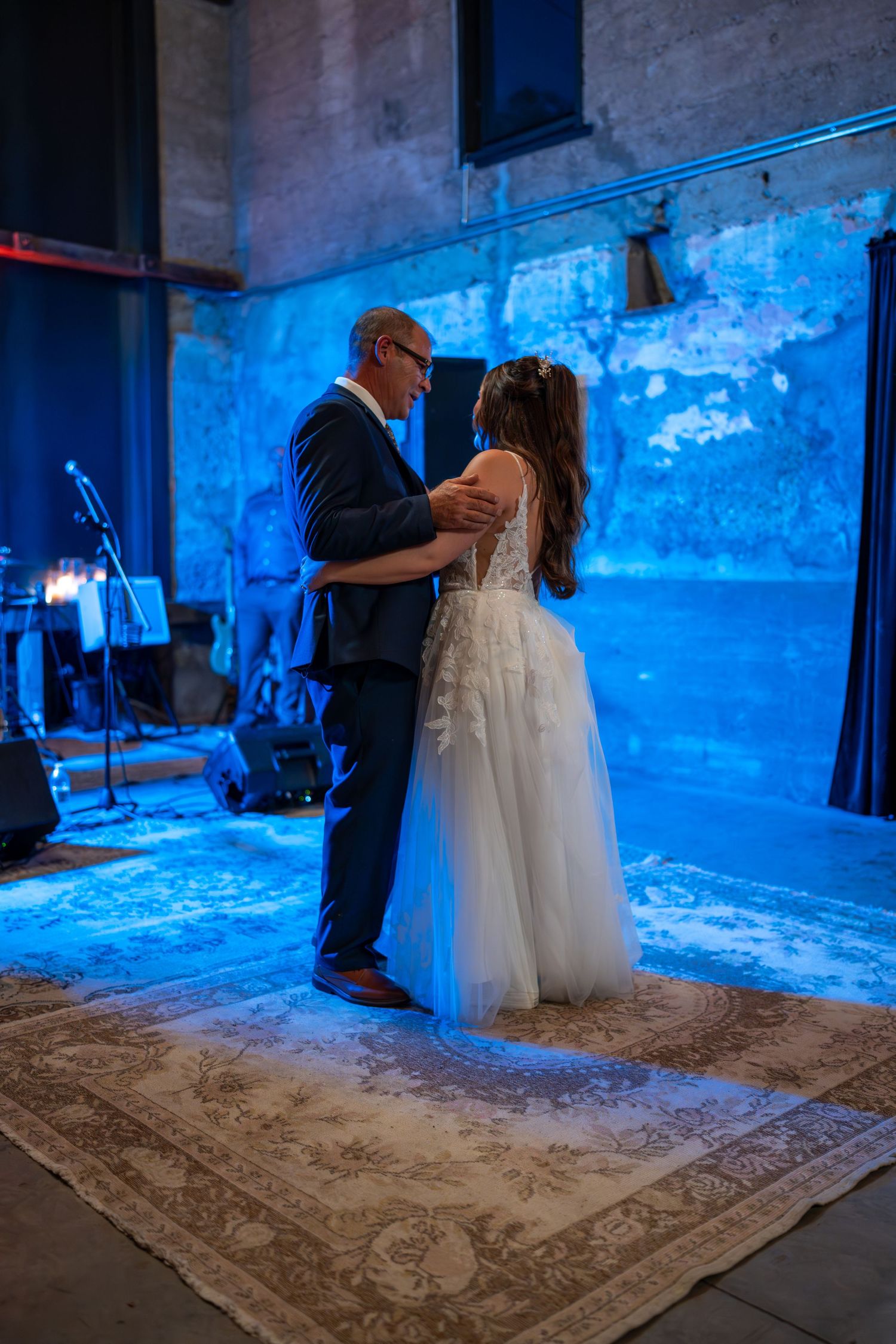 Bride and father share emotional first dance under blue lighting at wedding reception.