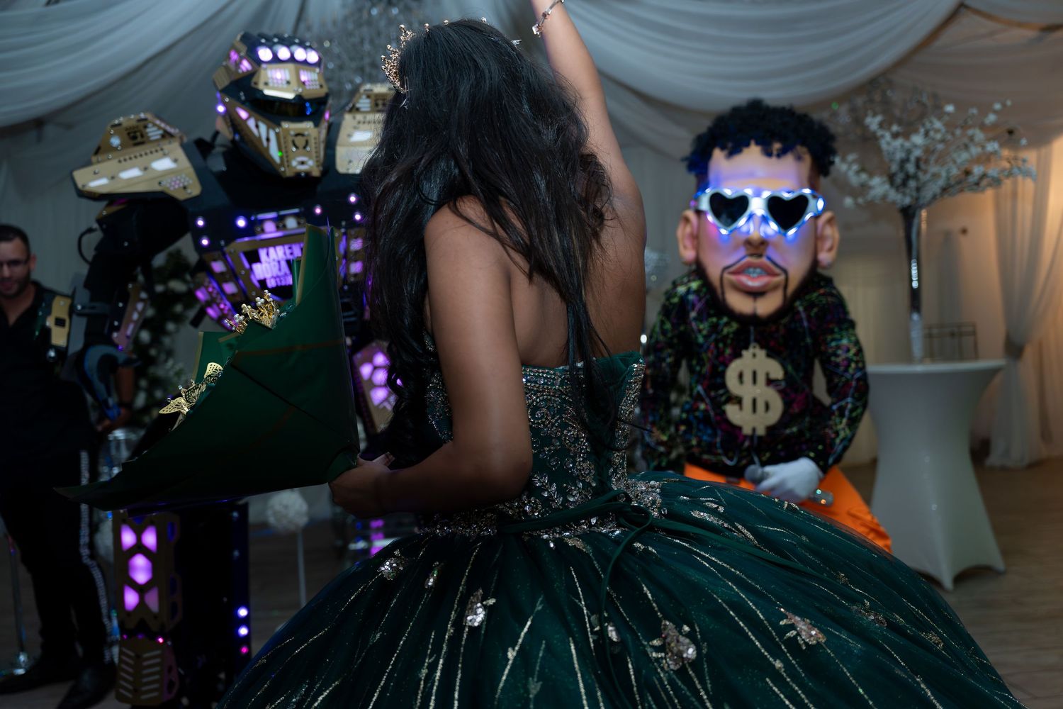 Girl in green quinceañera gown dances with costumed performers at a festive party celebration.