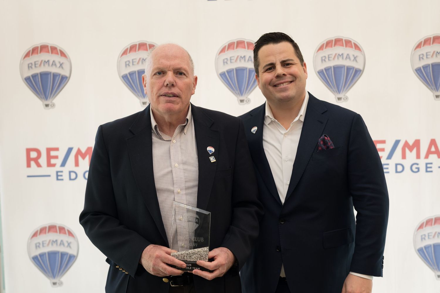 Two RE/MAX Edge real estate agents pose with crystal award at professional recognition event.