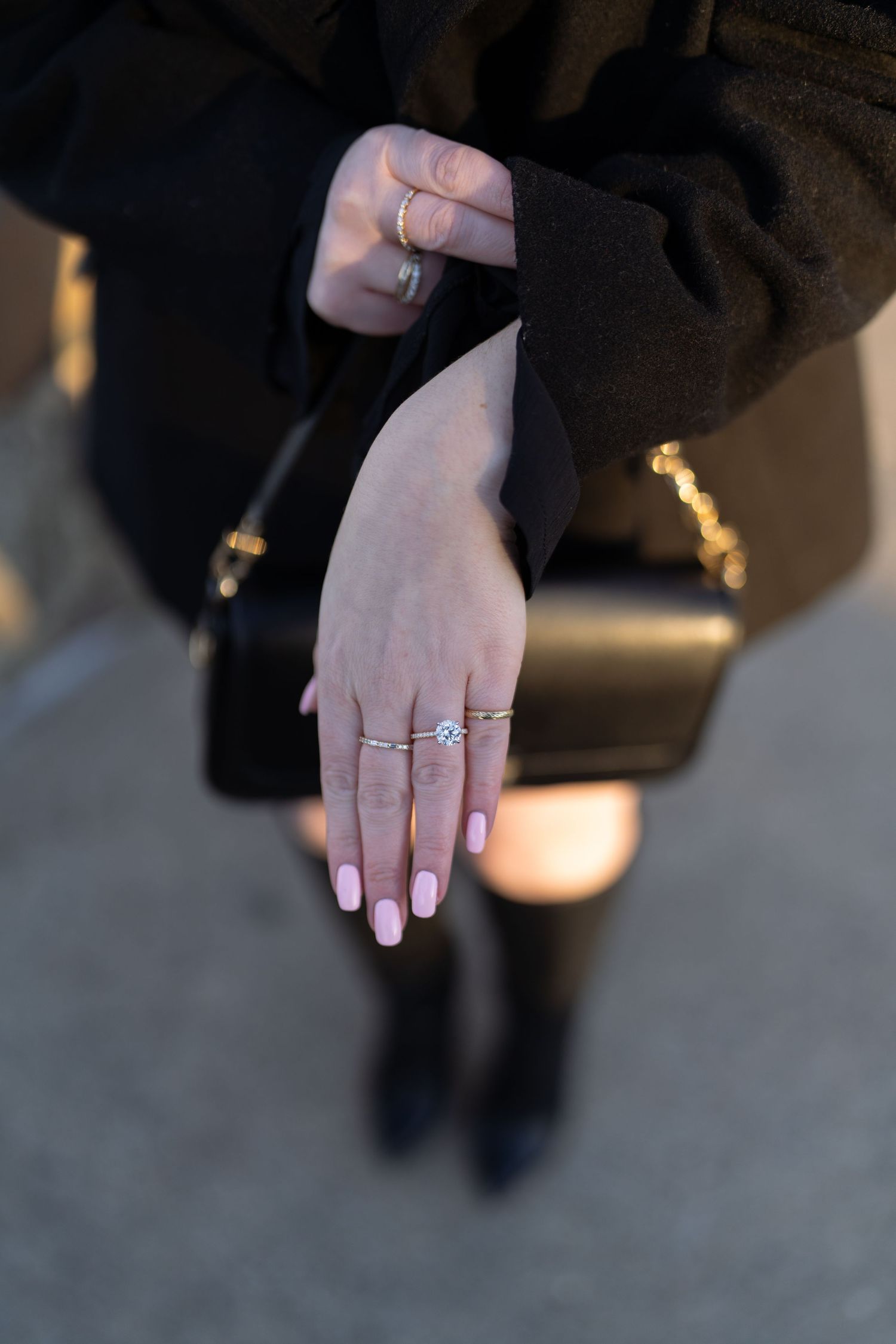 Close-up of woman's hand displaying a sparkling diamond engagement ring with pink manicured nails.