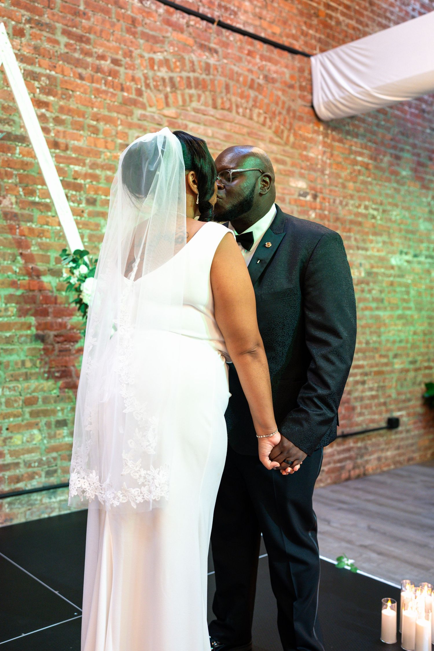 A bride and groom share their first kiss at the altar in a rustic brick-walled venue.