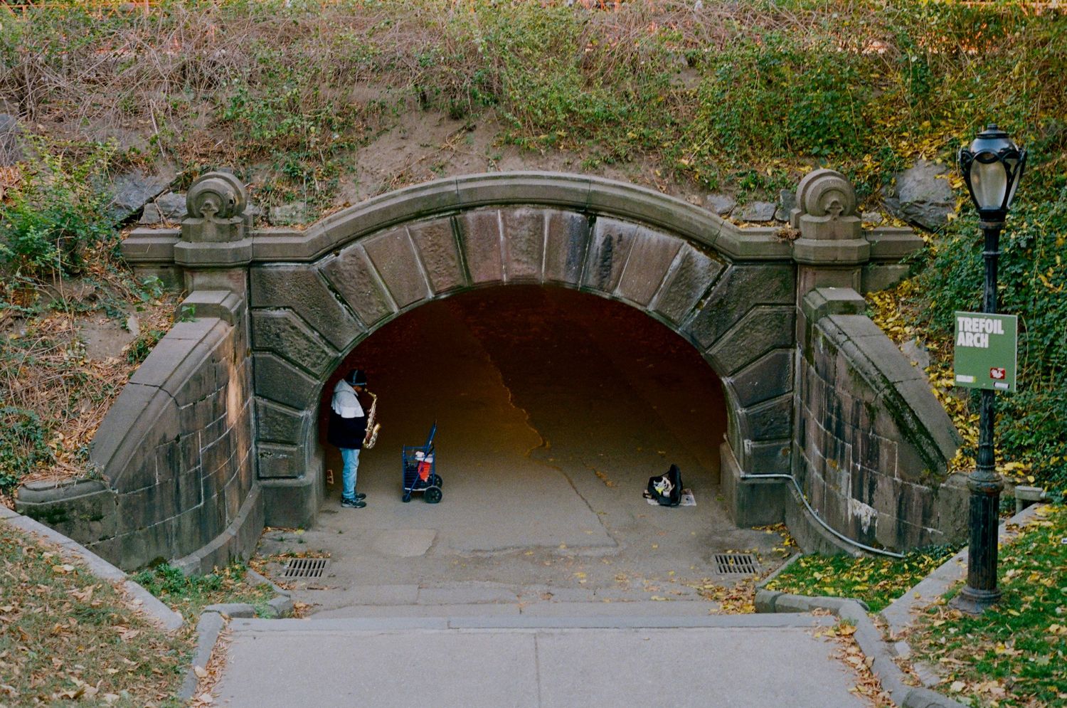 Stone arch tunnel entrance in Central Park with people walking through during autumn season in New York City.