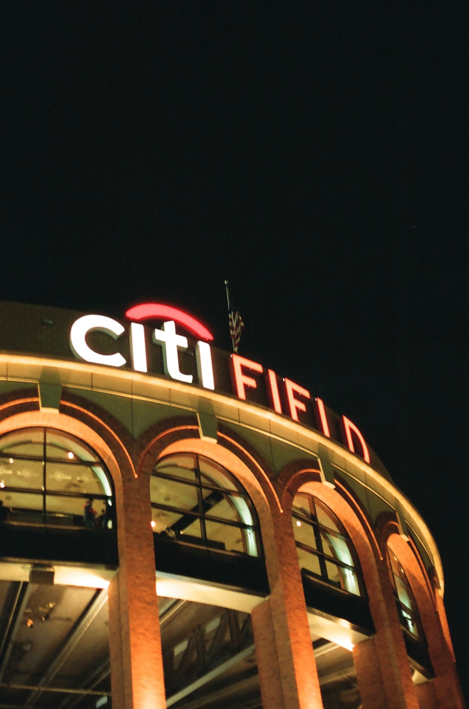 Citi Field baseball stadium exterior with illuminated red and white sign at night.