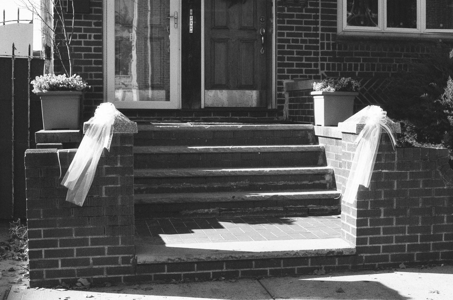 Black and white photo of brick front steps decorated with white bows at a home entrance.
