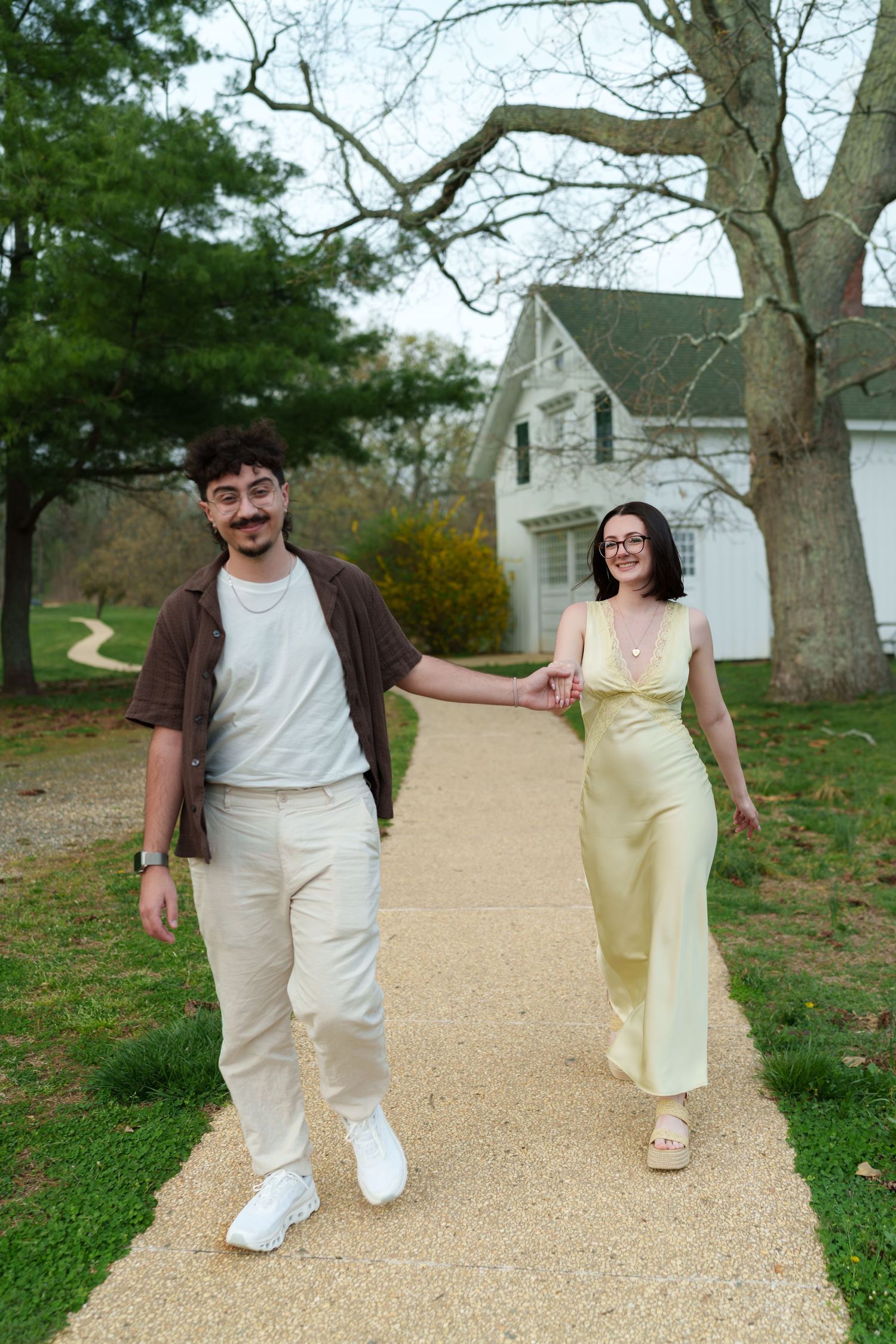 Happy couple walking hand in hand along a garden path near a classic white country home.