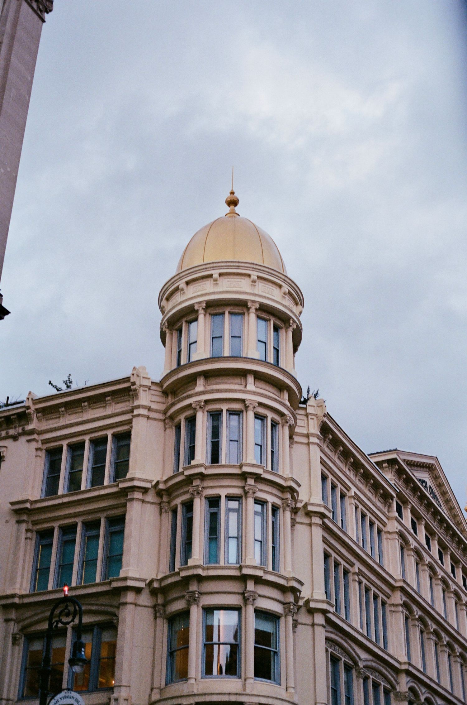 Historic beige building with ornate dome topped with gold finial against cloudy sky.