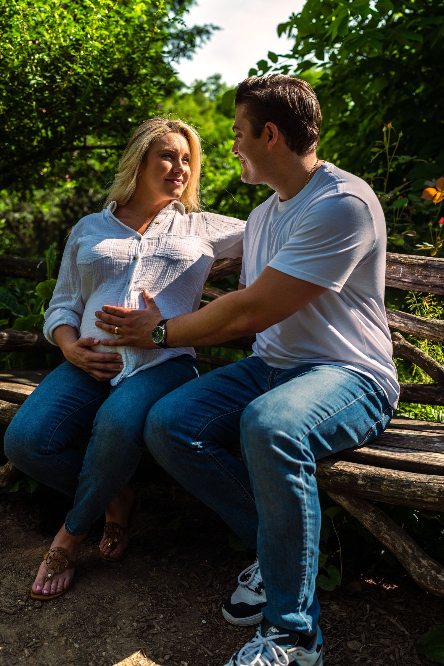 Expecting couple sitting on a rustic bench in a lush green park, smiling.