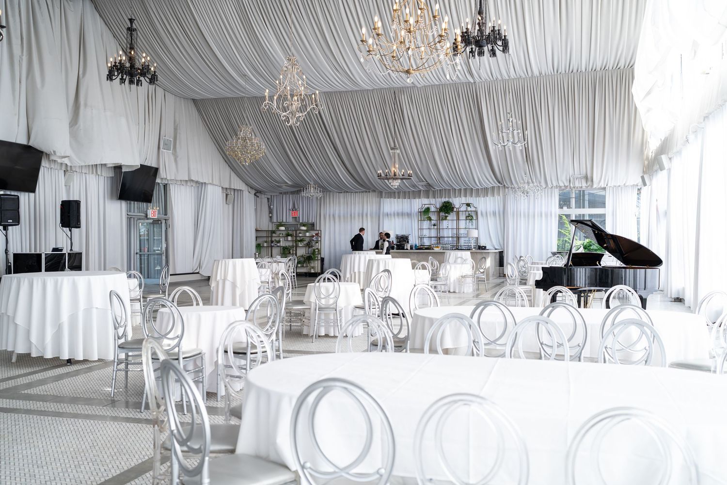 Luxurious white draped wedding reception hall featuring crystal chandeliers and a black grand piano.