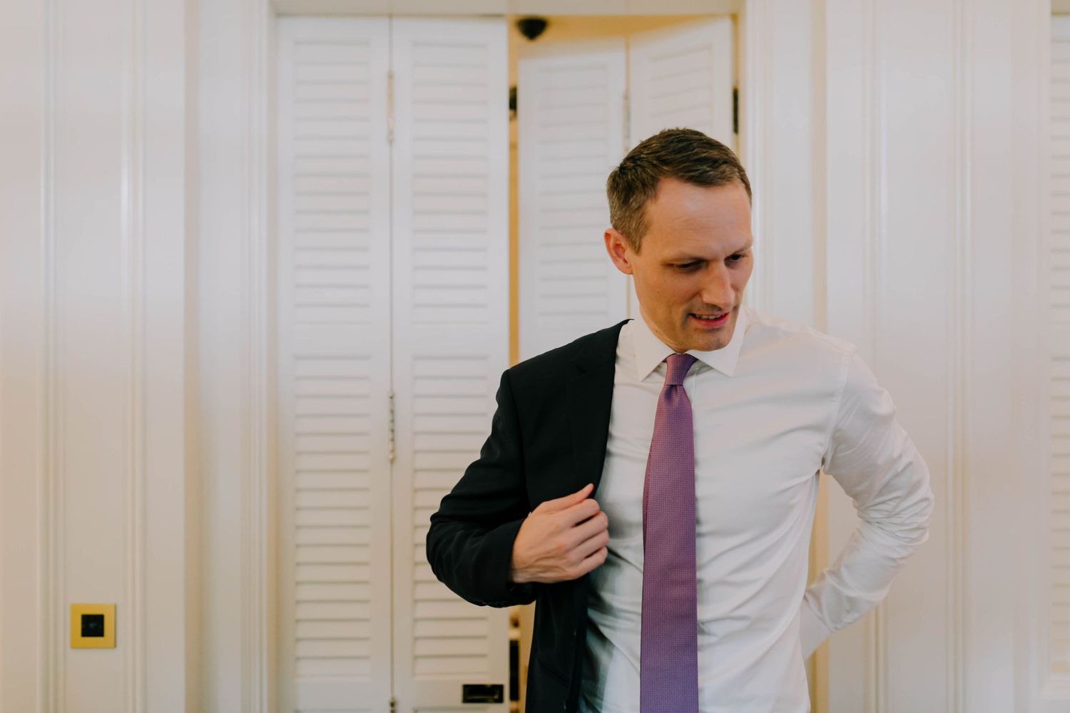 groom putting on suit jacket for wedding at raffles hotel singapore