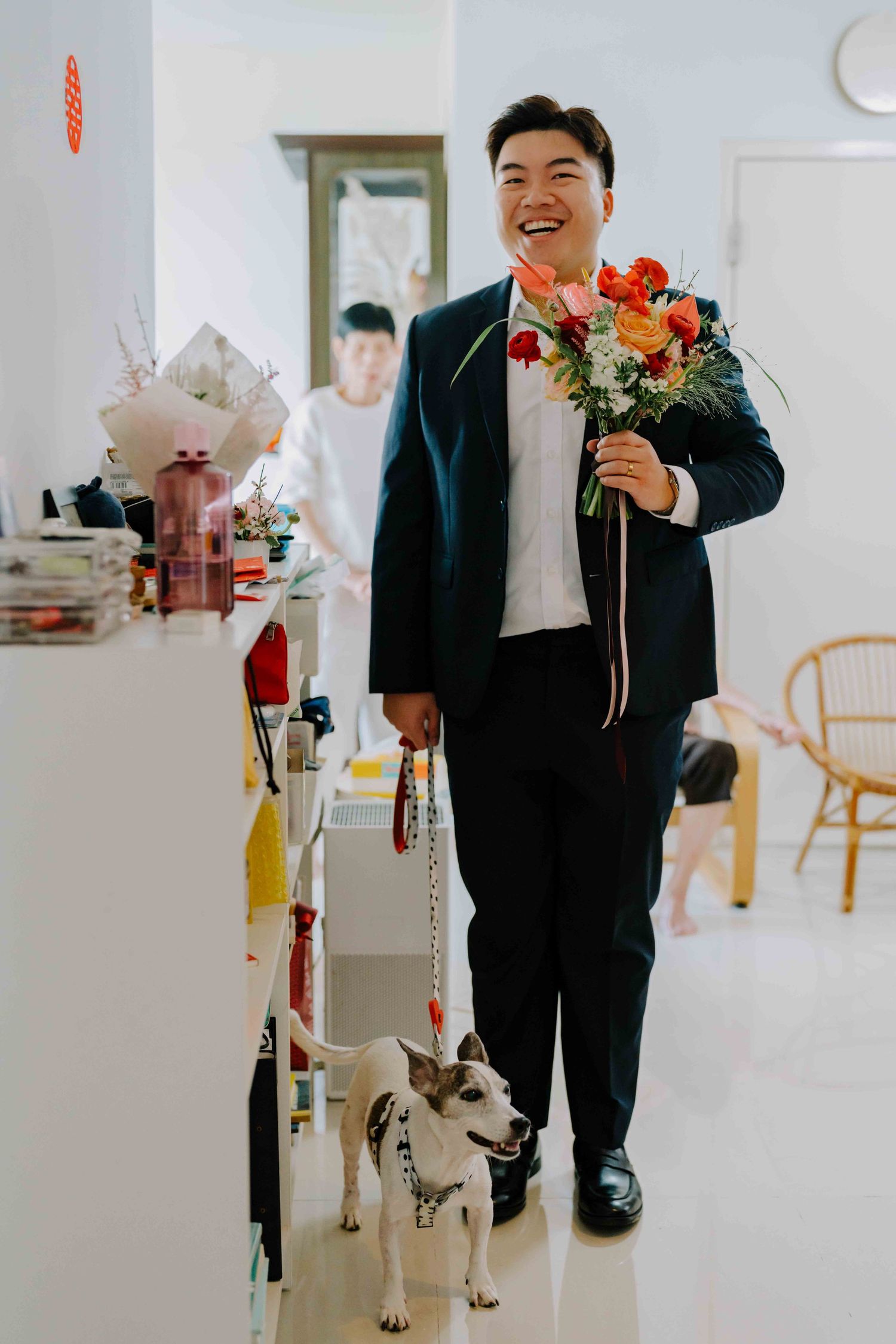 groom holding a wedding bouquet for his bride with their pet dog