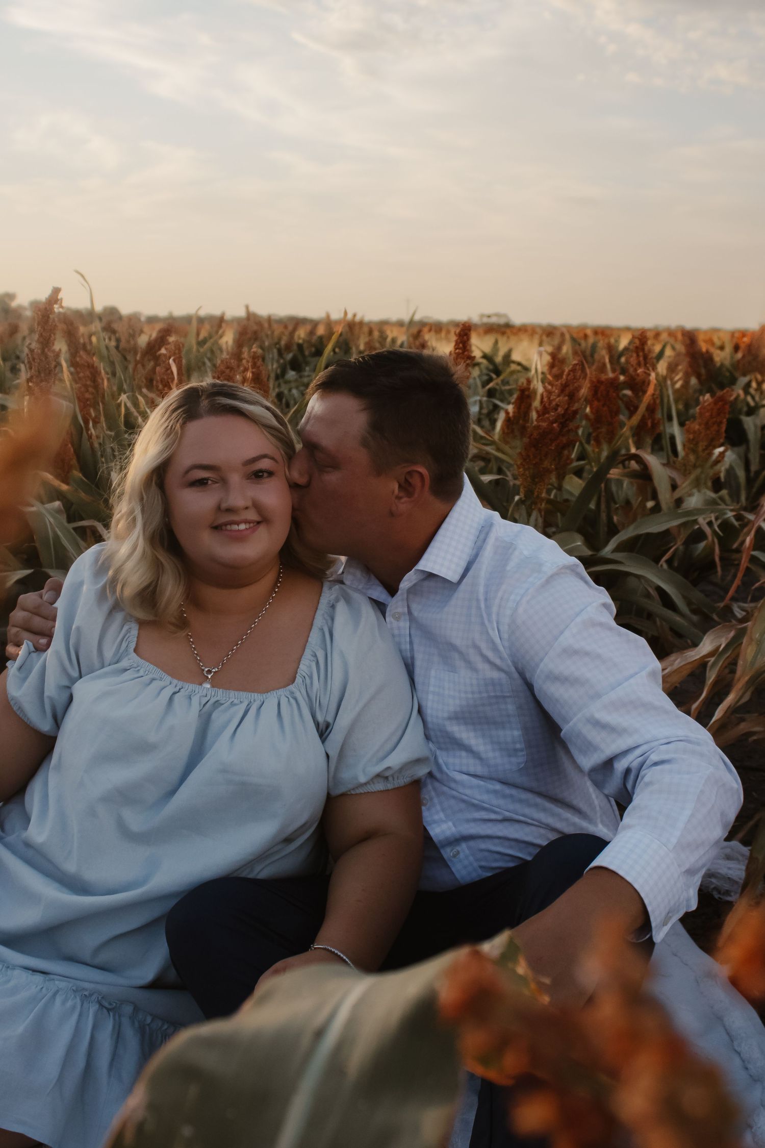 A romantic couple shares tender moments while sitting together in a golden cornfield at sunset.