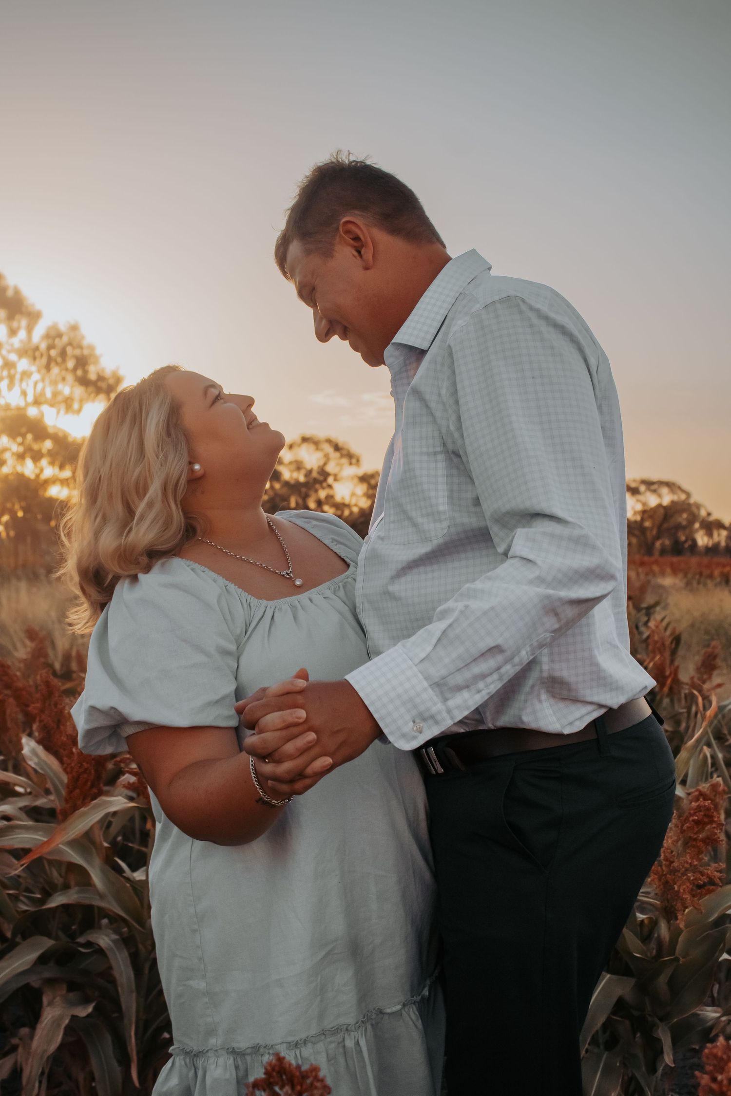 Romantic couple embraces in a sunlit field during sunset creating silhouettes against the golden sky.