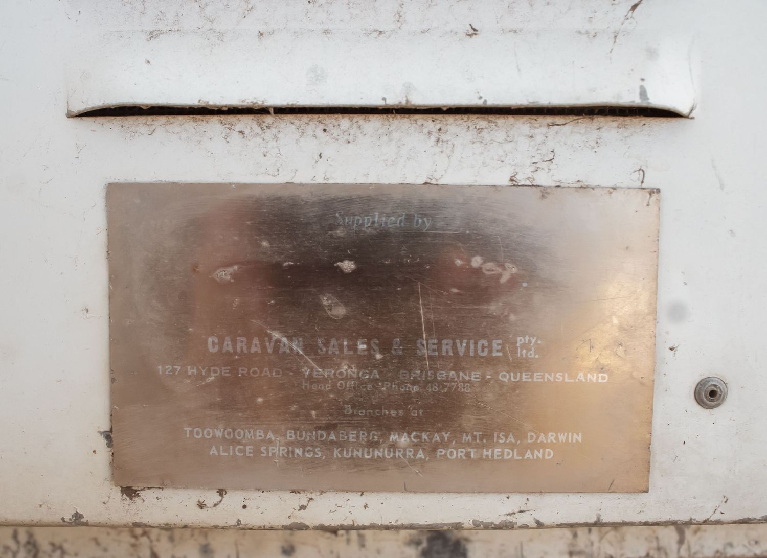 A series of vintage metal plaques or nameplates mounted on a white wall showing weathered text and patina.