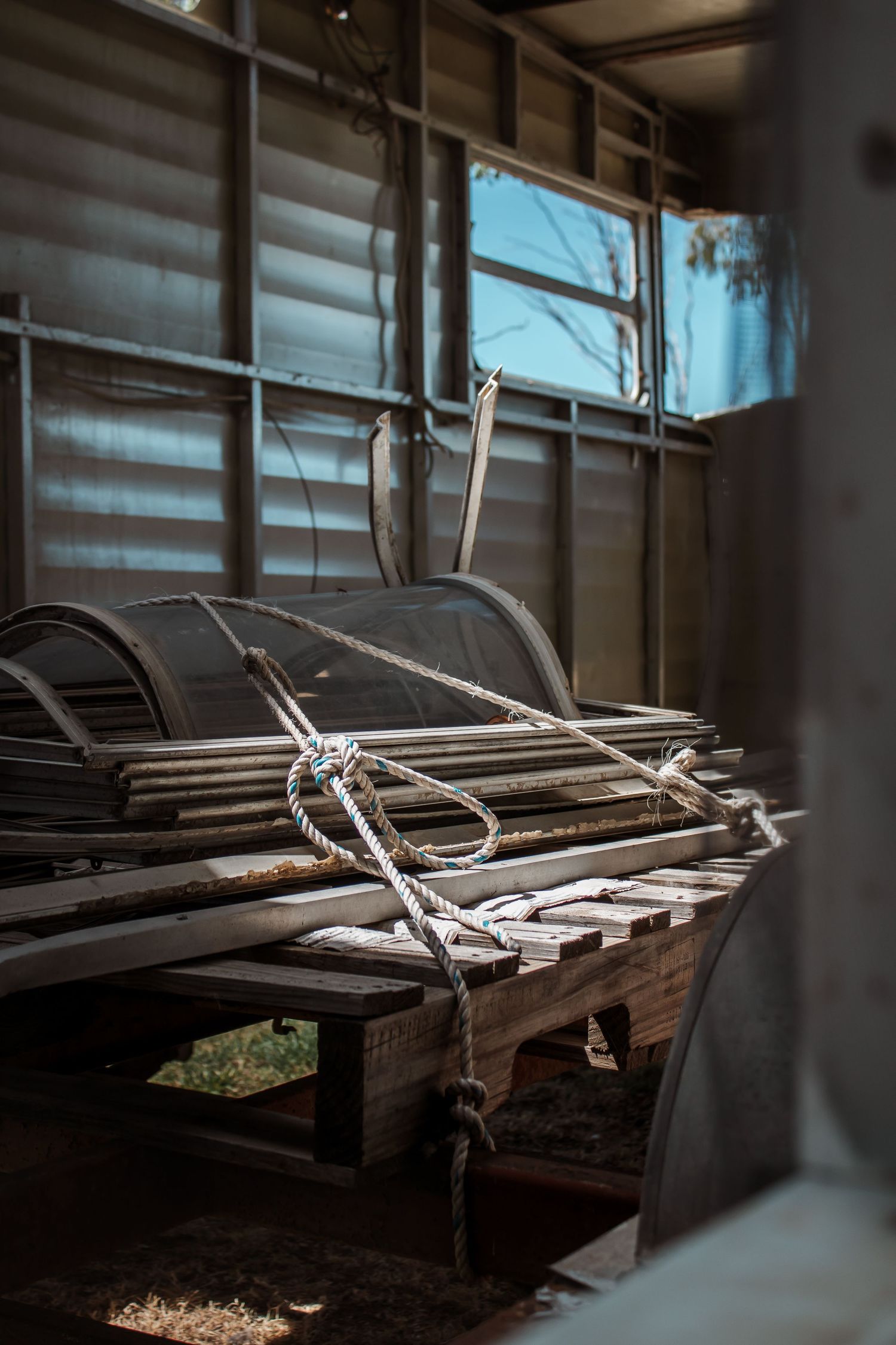 Old wooden slats tied together with rope create a rustic shelf or storage structure in a dimly lit space.
