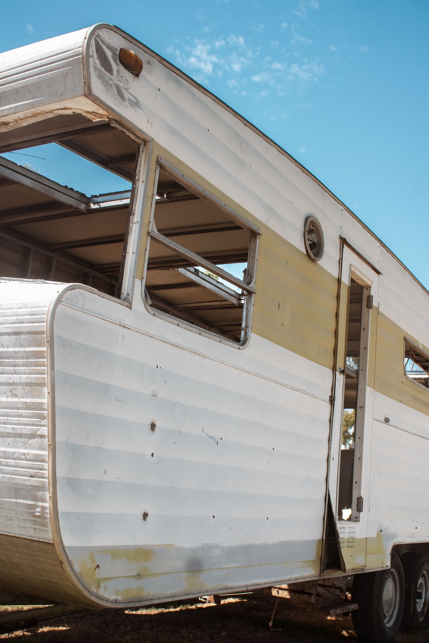 Side view of a white vintage travel trailer showing multiple windows and exterior panels against a blue sky background.