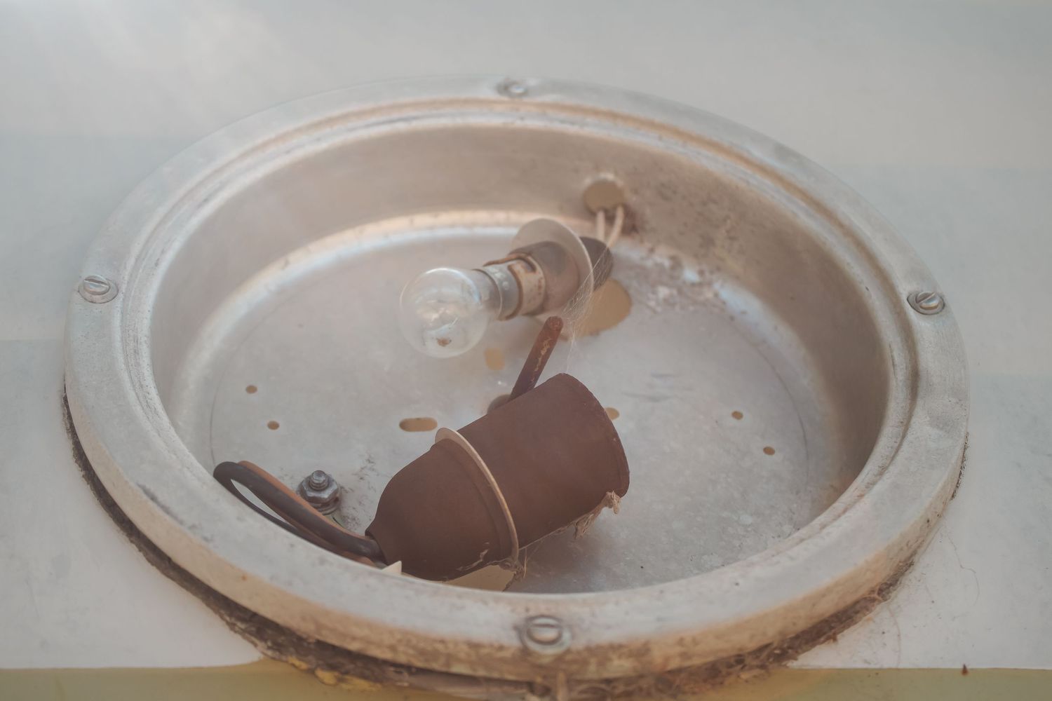 A broken light bulb lies in a circular glass fixture with water droplets and condensation.