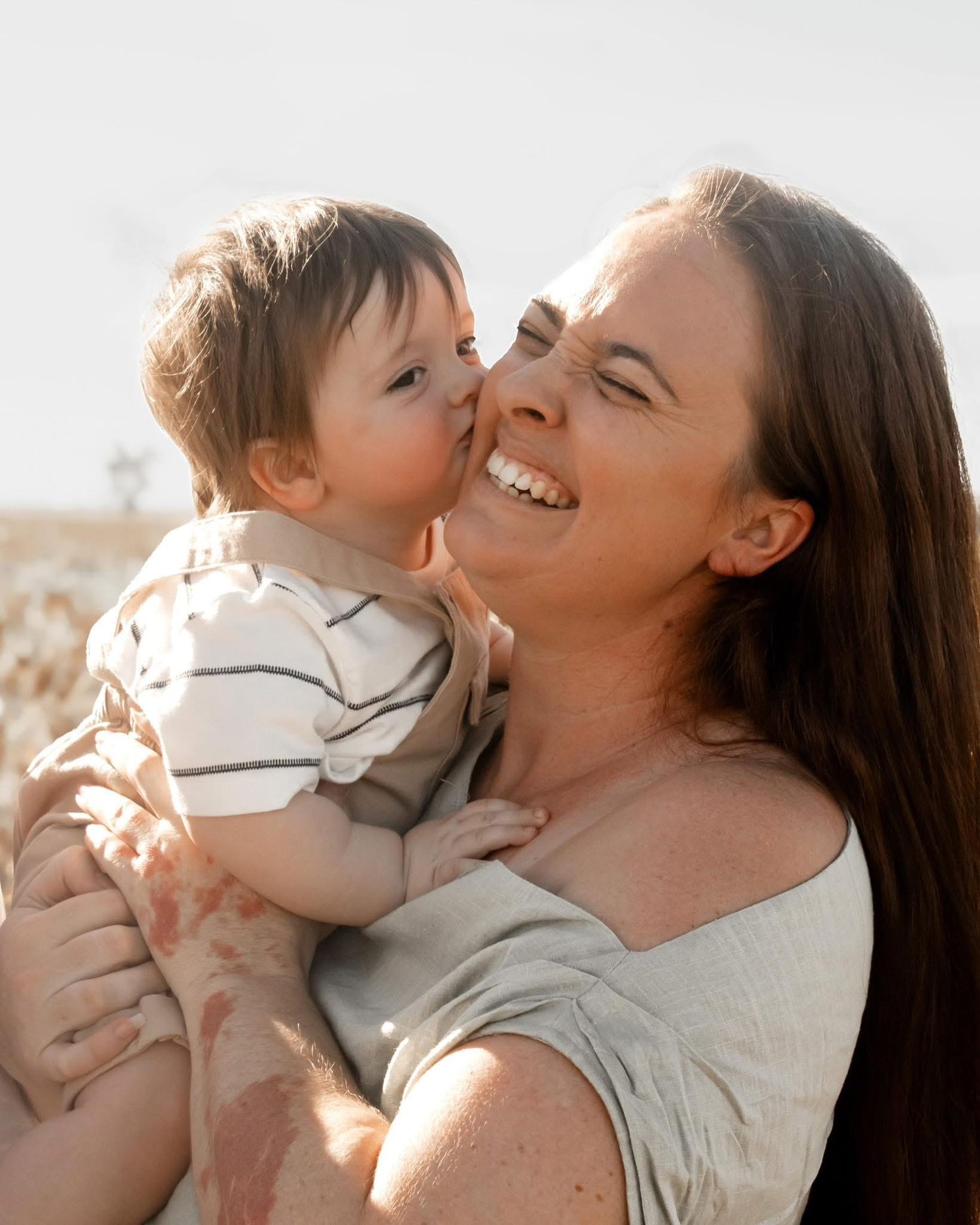 A tender moment of affection and laughter captured in warm sunlight between parent and child.