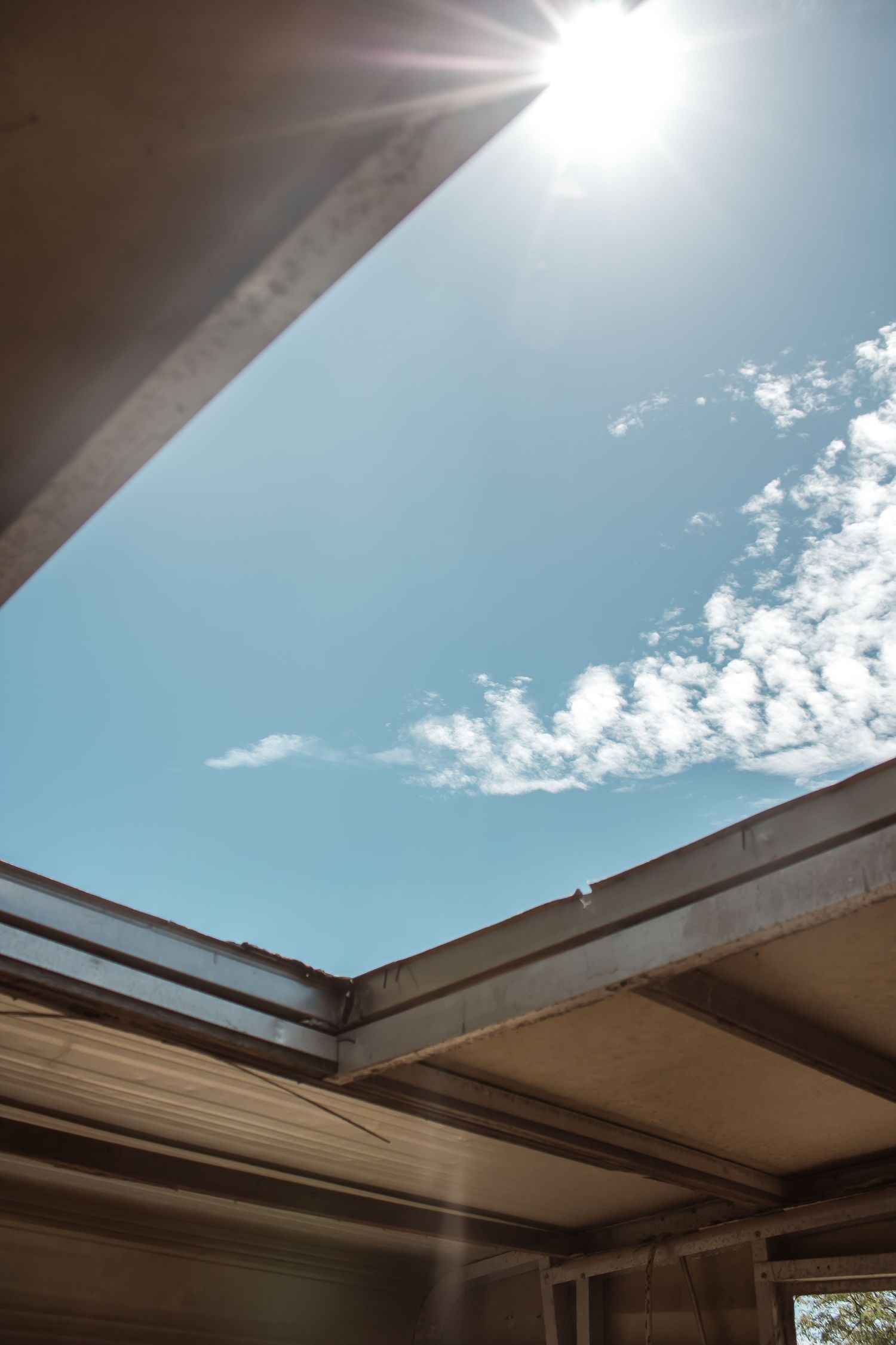 Sunlight streams through an open skylight in a modern building, creating dramatic rays against a bright blue sky.