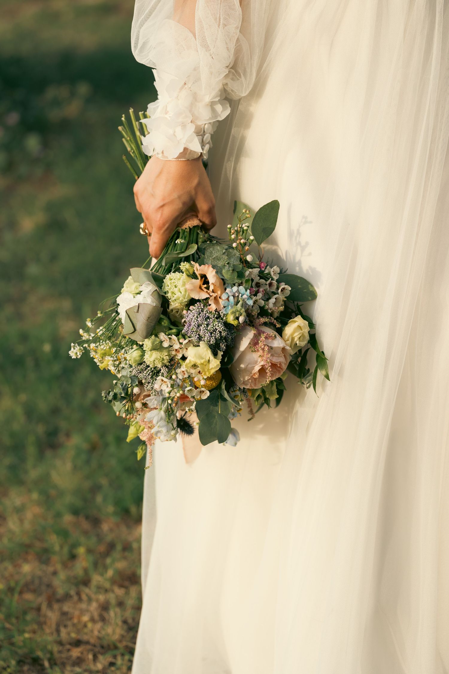 Beautiful bridal bouquet with eucalyptus, roses and mixed flowers against white wedding dress.