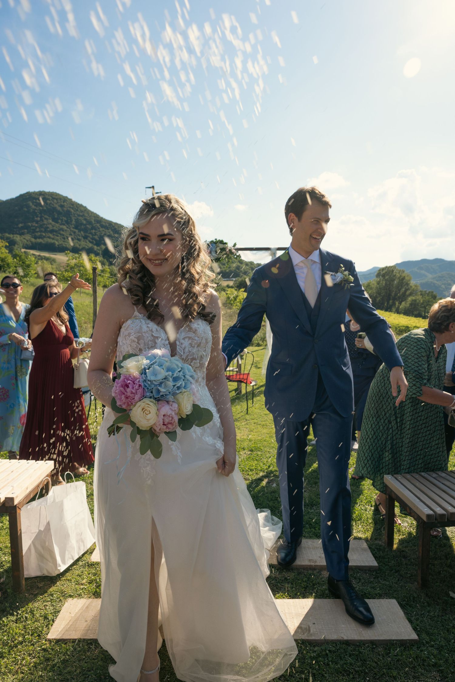 Couple celebrates joyfully in an outdoor wedding ceremony with mountain views and guests throwing confetti.