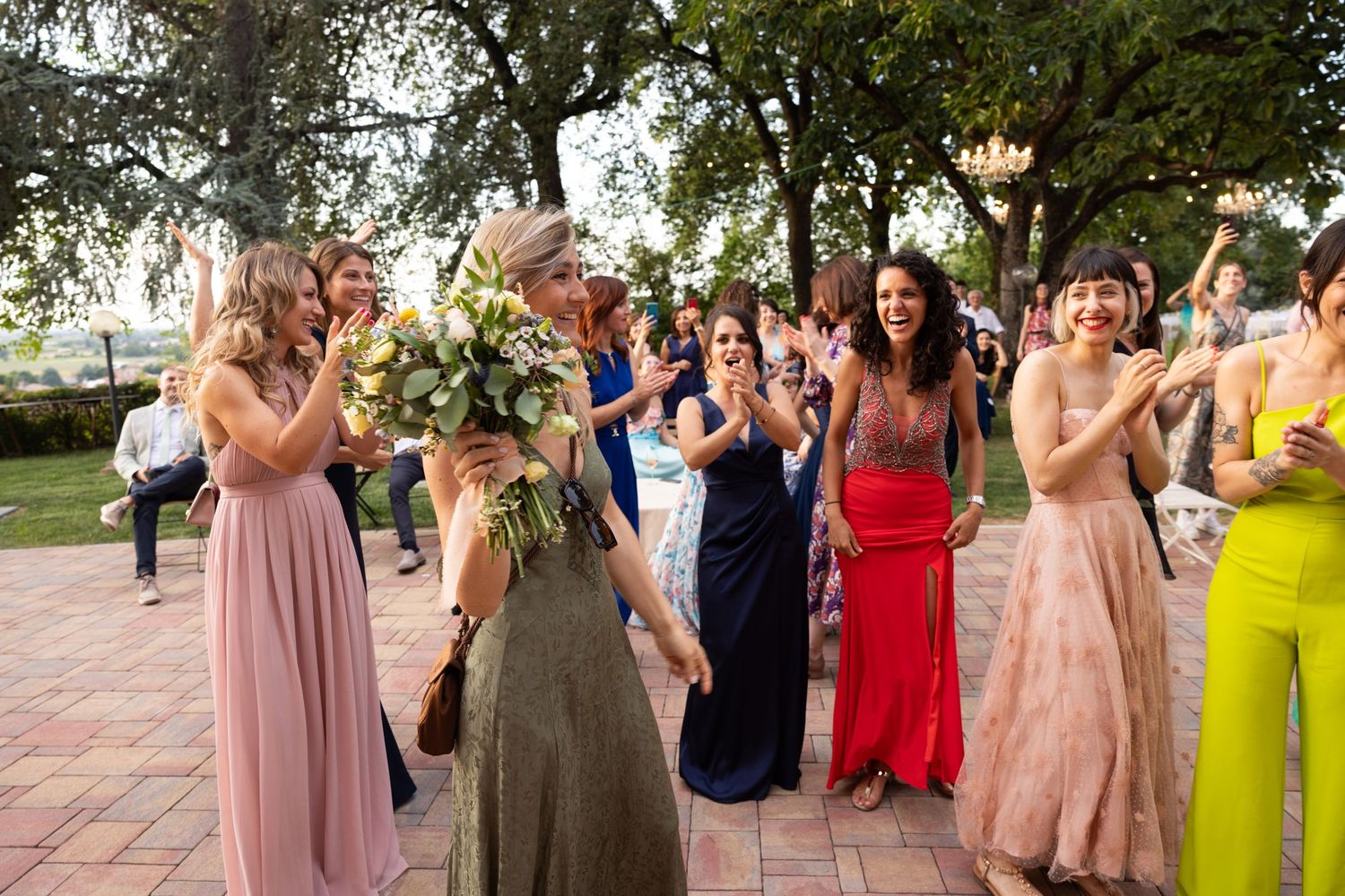 Wedding party in pastel and bright colored dresses posing together outdoors.