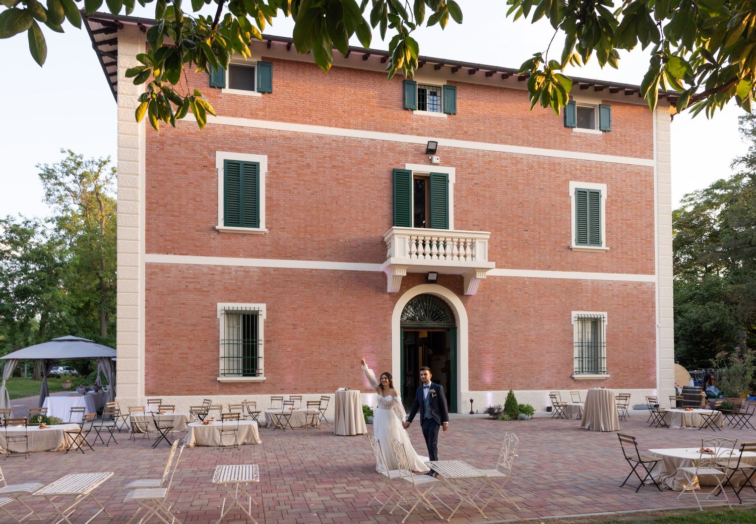Elegant brick villa exterior with arched doorway and terrace during a wedding celebration.