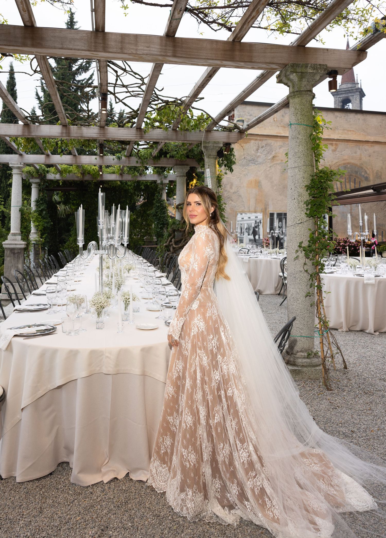 Elegant wedding reception venue with white tablecloths and rustic wooden pergola decorated with hanging greenery.
