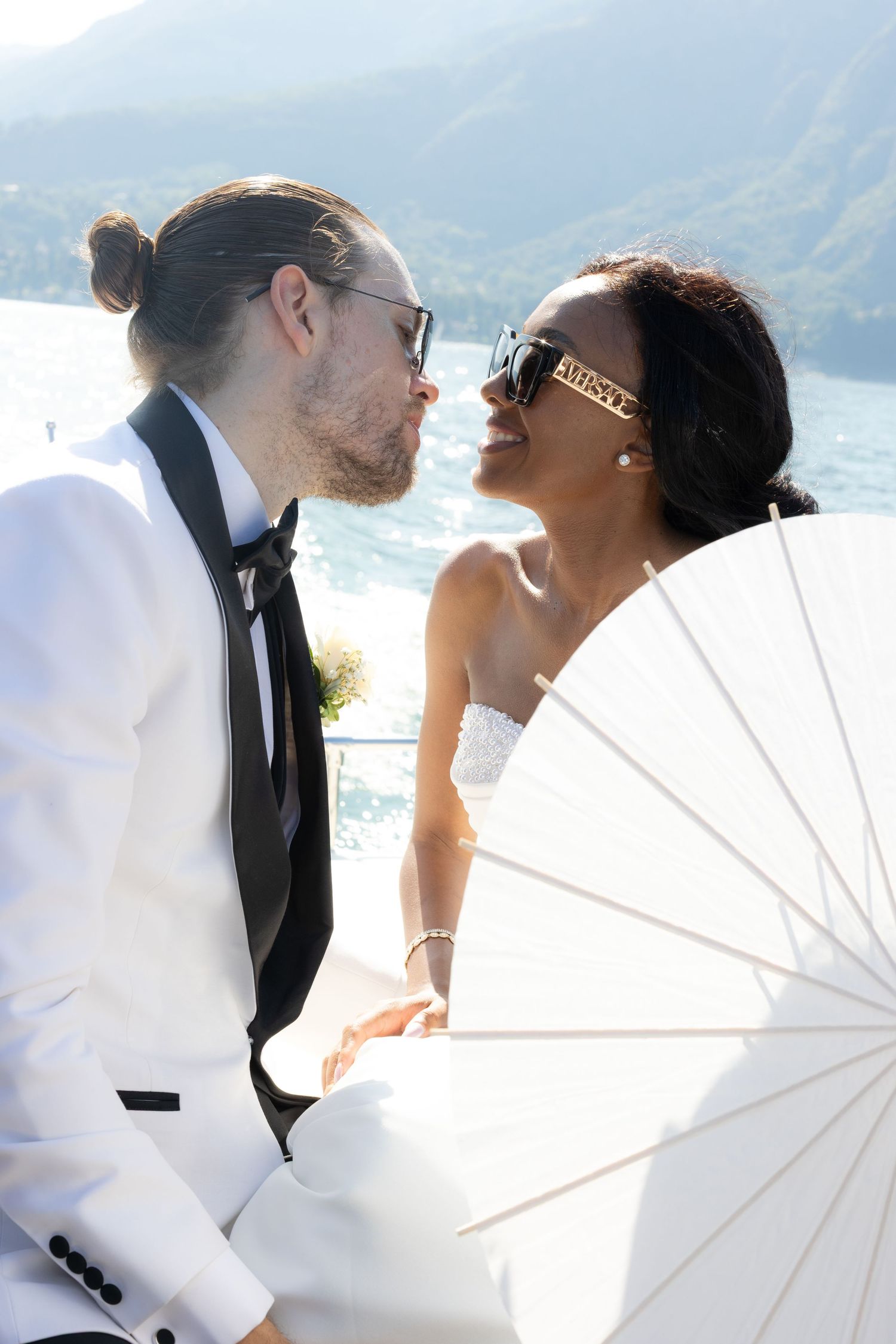 Romantic newlyweds share intimate moments under white parasols against a scenic mountain lake backdrop.