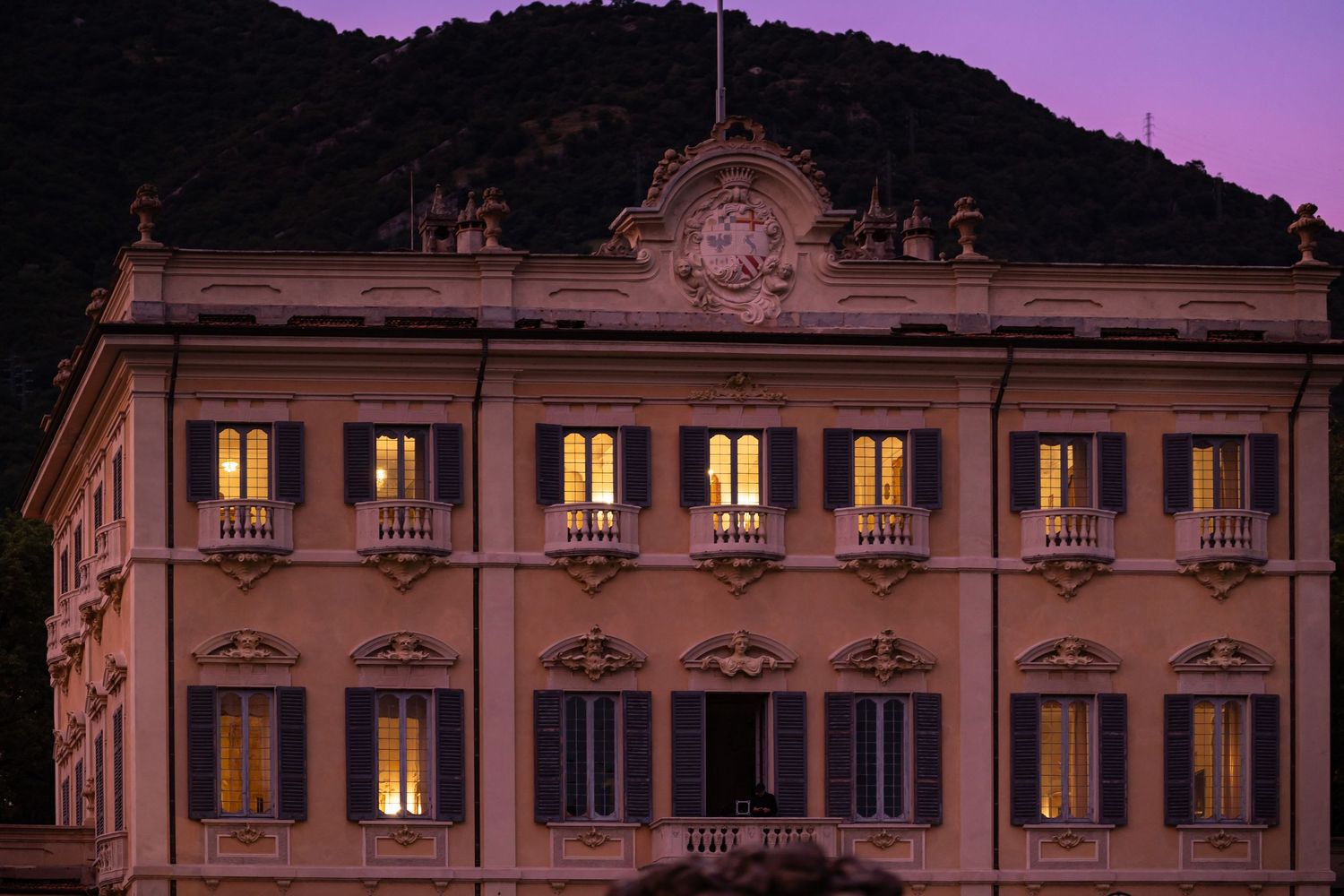 Historic villa facade at sunset with illuminated windows and ornate architecture.