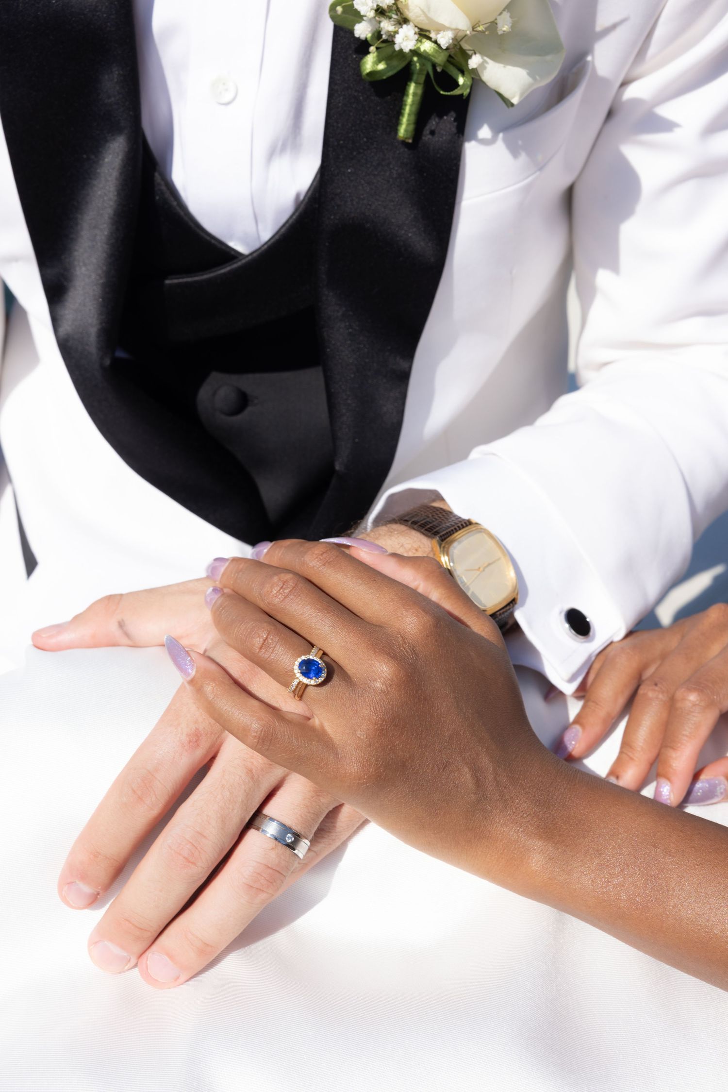 Close-up of hands wearing wedding rings and formal attire in black and white during a ceremony.