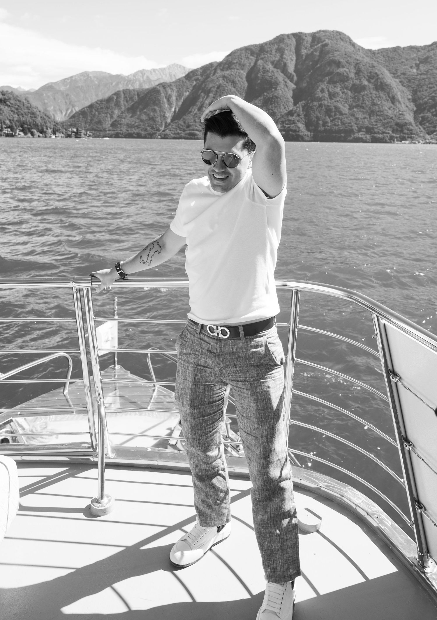 Person enjoying a sunny day on a boat deck with mountains in the background.