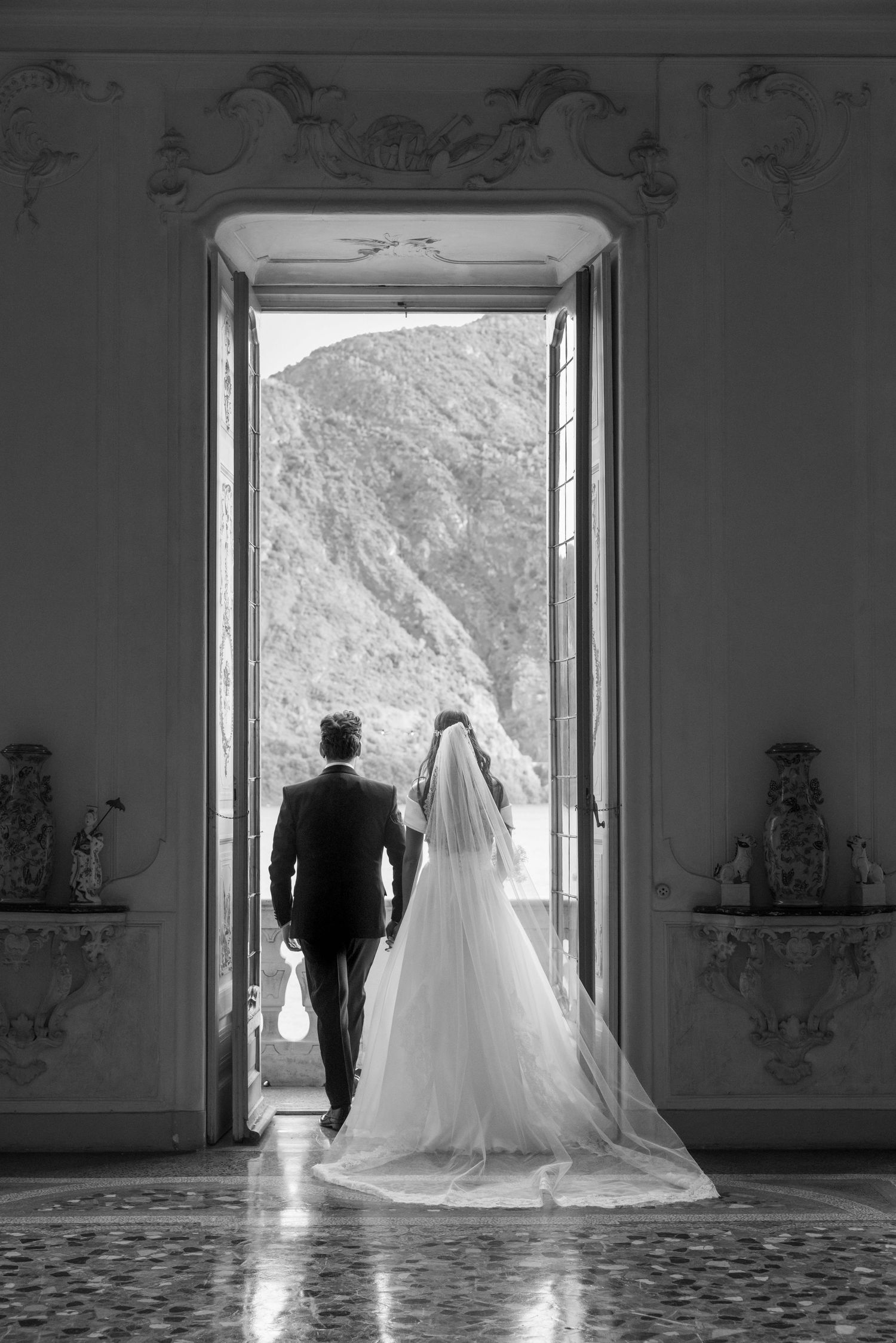 Dramatic black and white photo of couple framed in doorway overlooking mountain landscape.