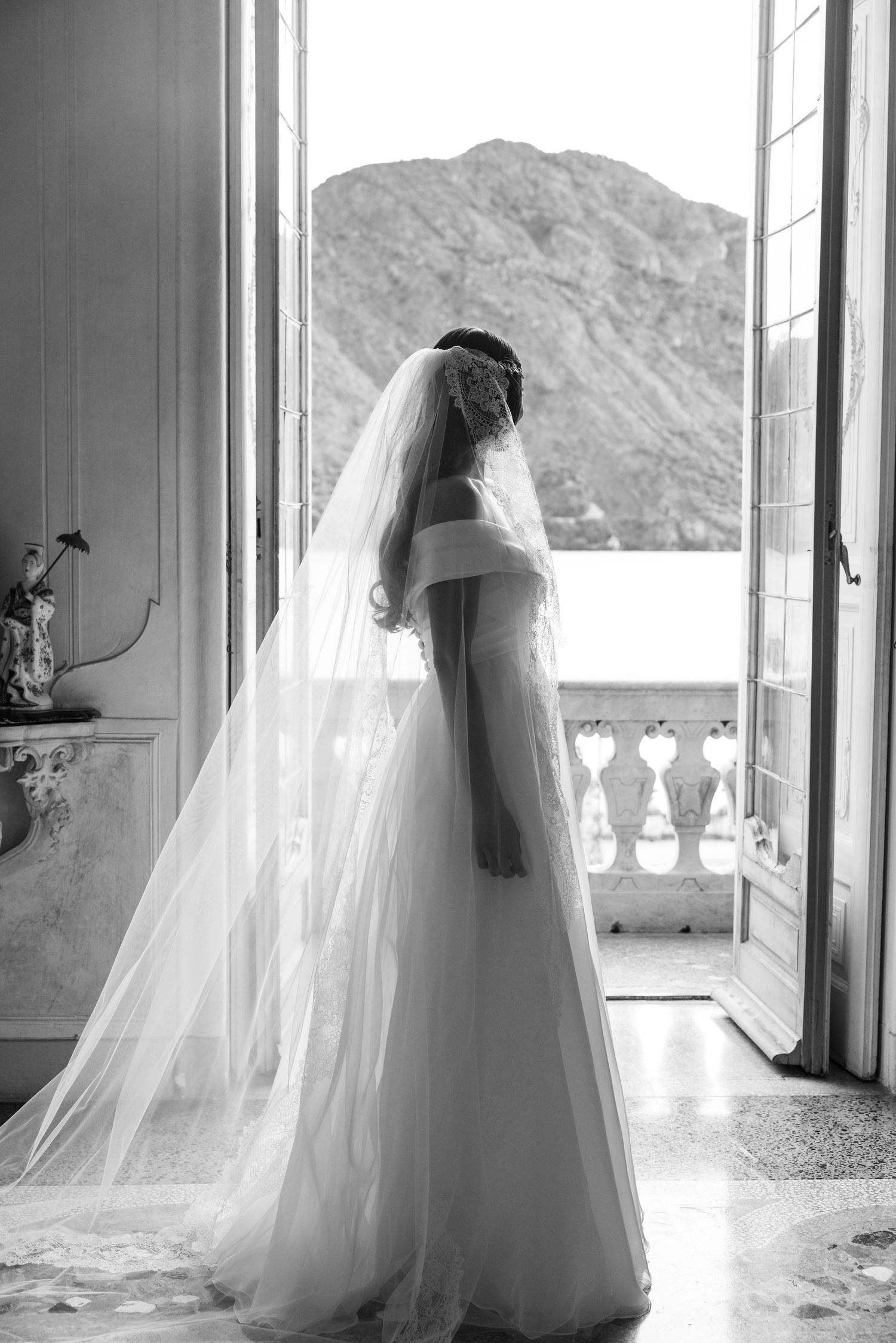 Sunlit bridal silhouette against mountain views through elegant French doors.