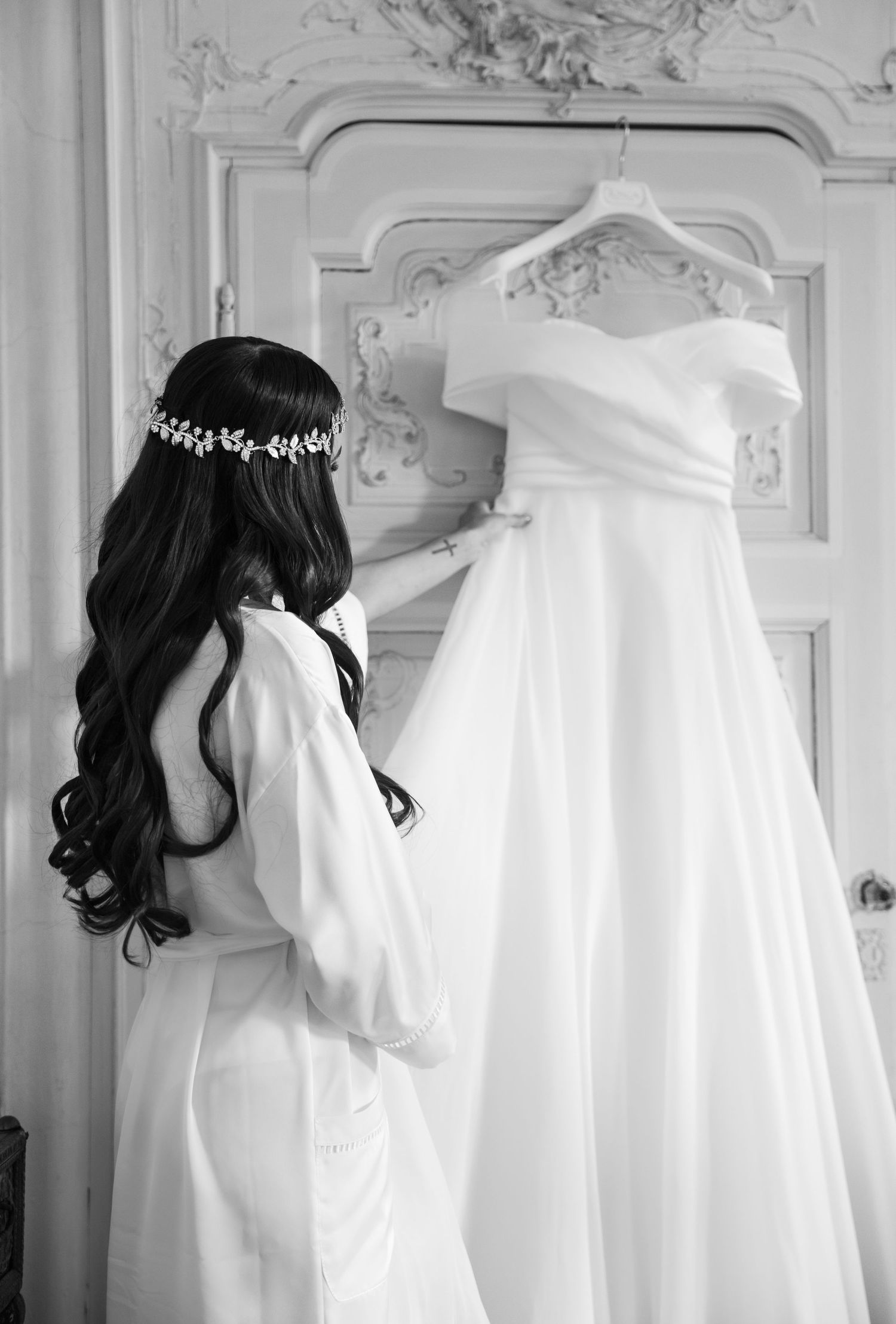 Black and white photo of wedding dress preparations in an ornate room.