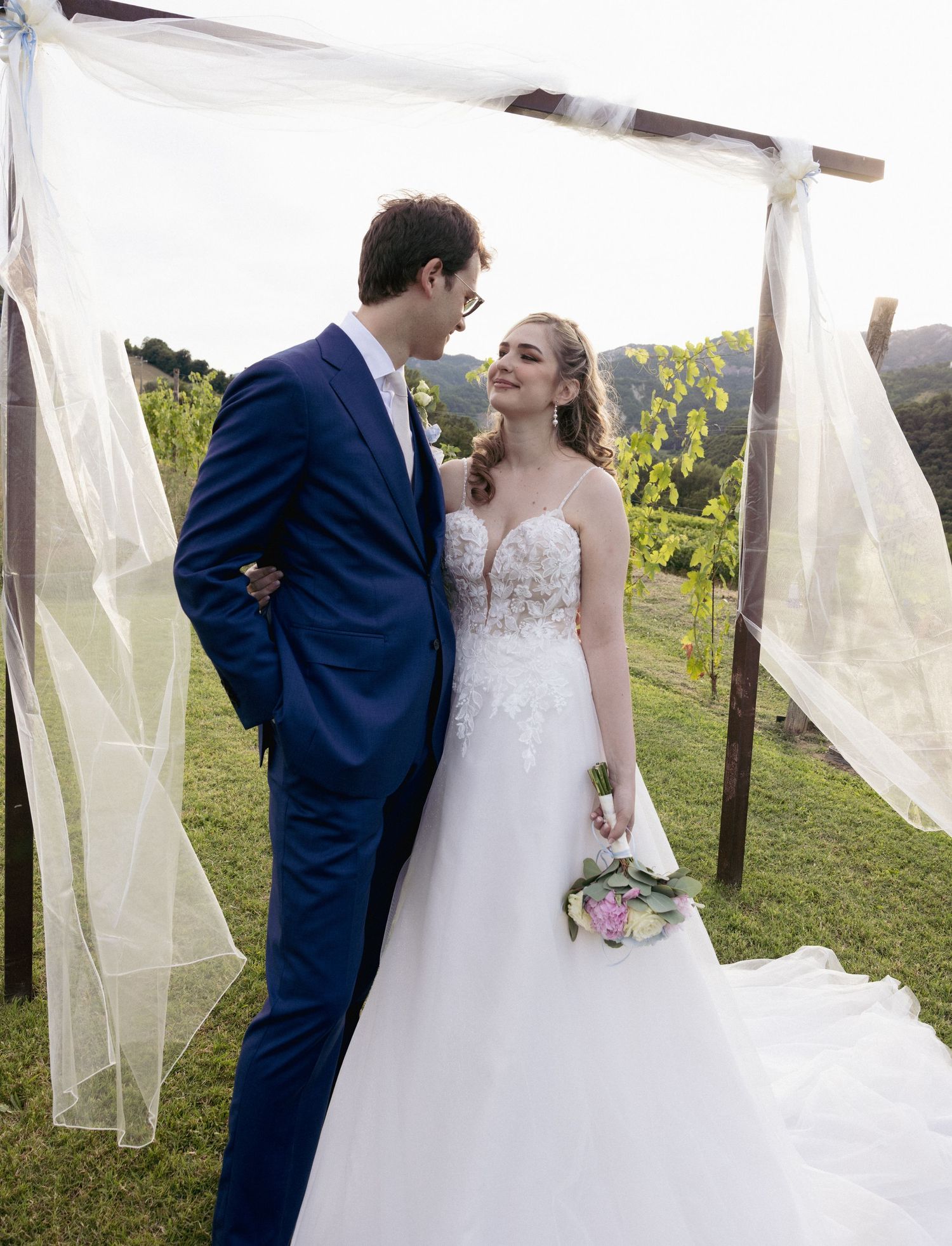 A couple posing among white fabric drapes in an outdoor vineyard setting.