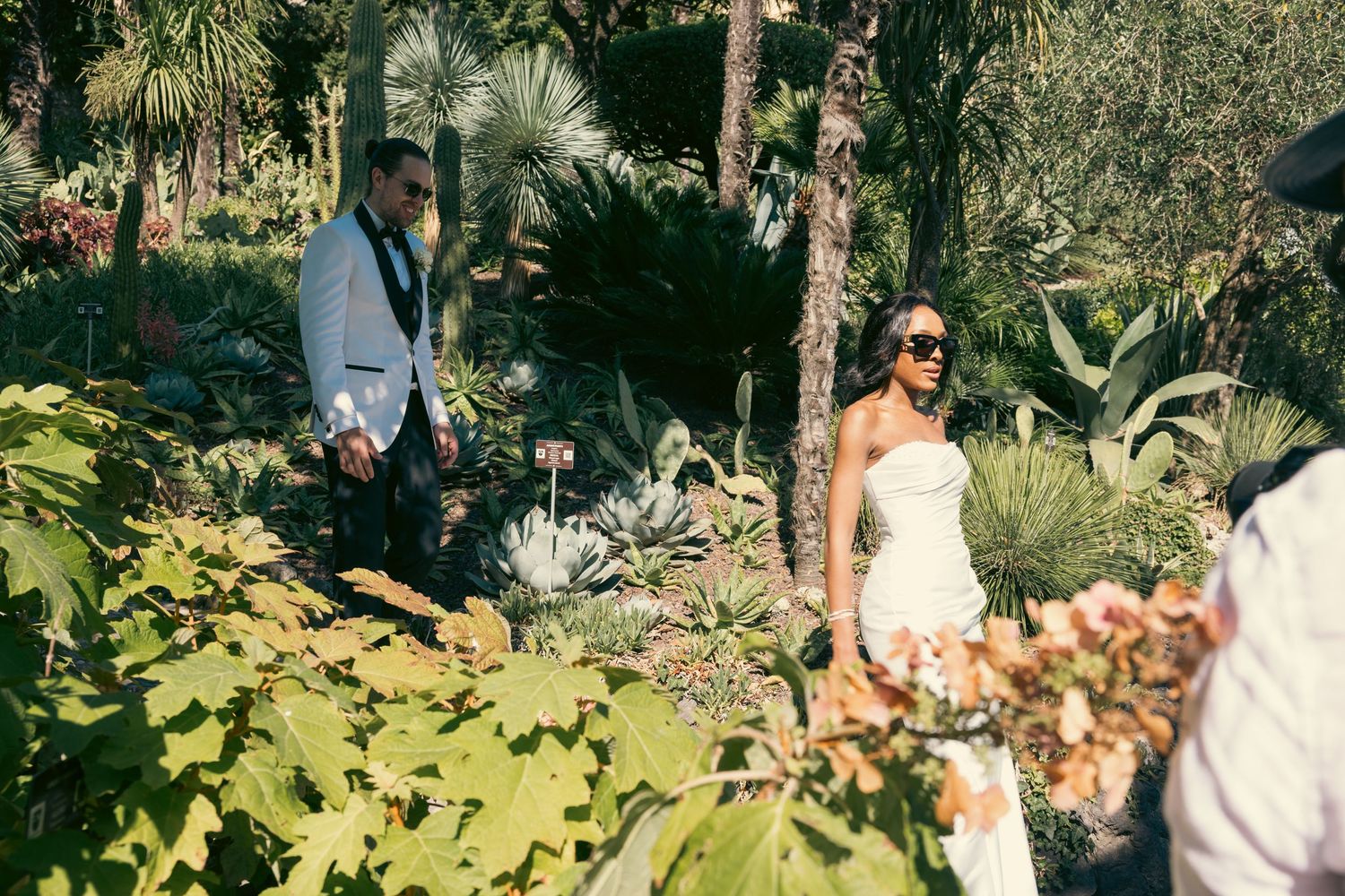 A lush garden setting with people enjoying an outdoor gathering among tropical plants and greenery.