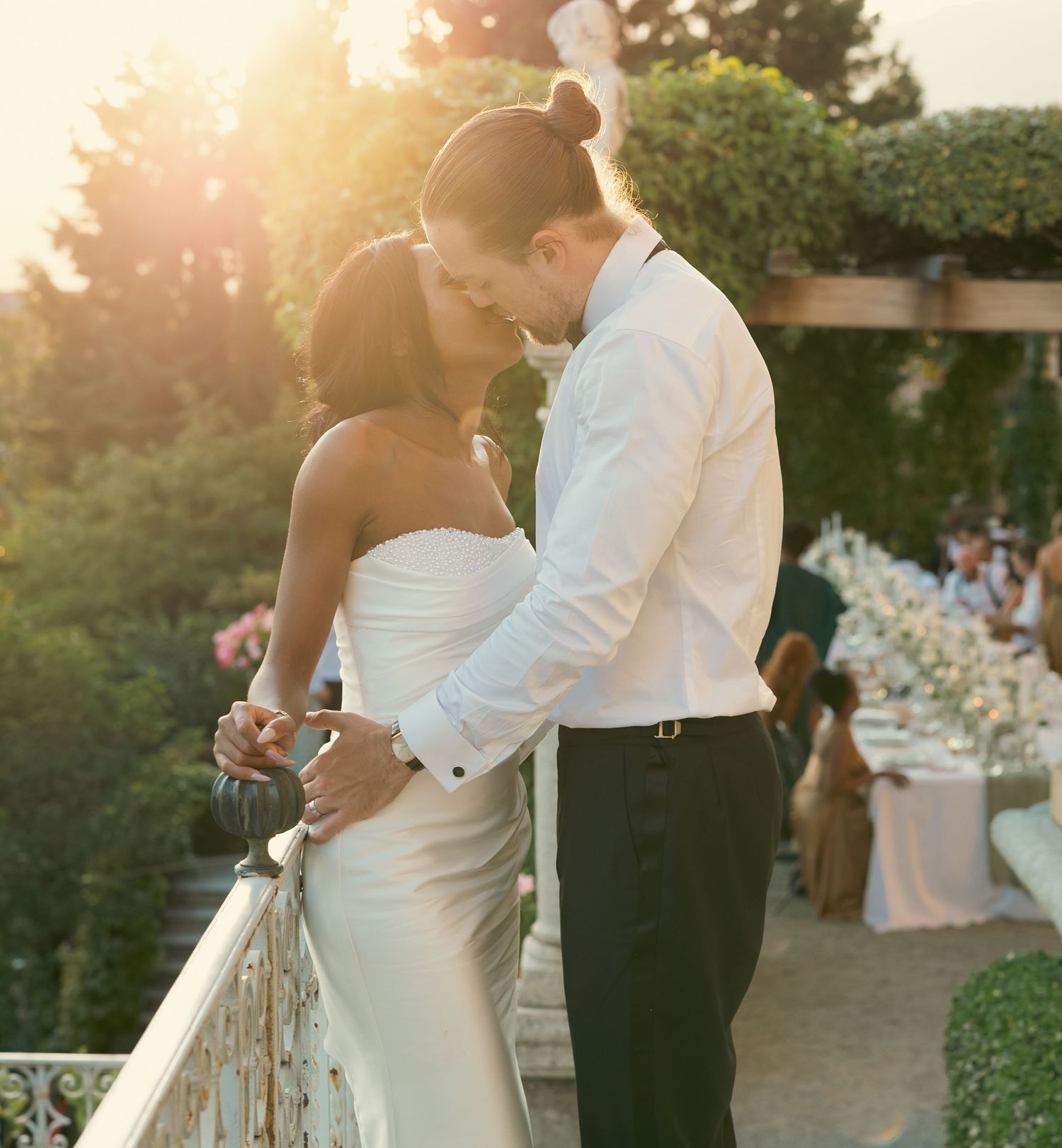 Couple embraces during golden hour at an outdoor wedding reception with floral decor and table settings.