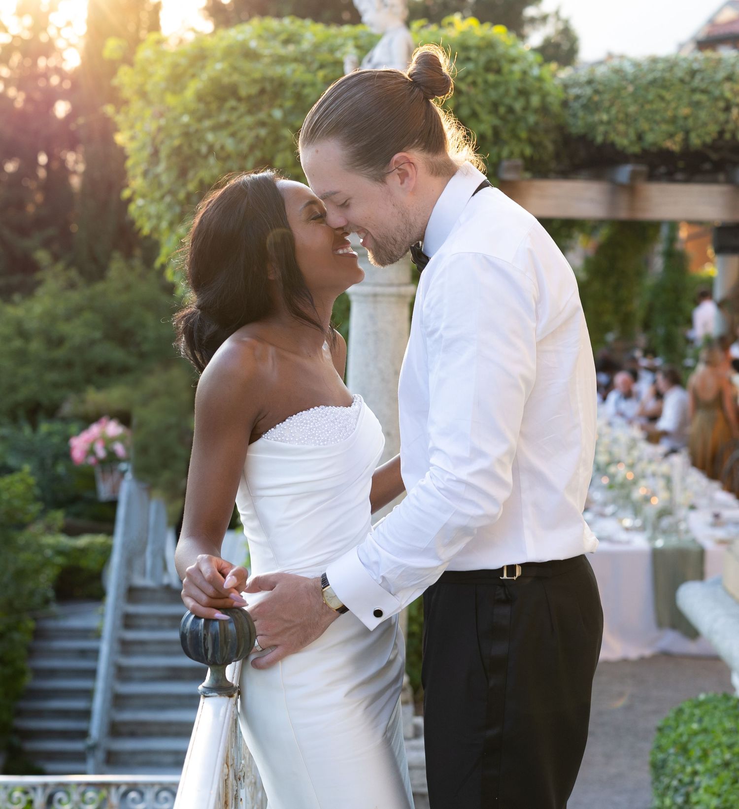 Couple dancing together at sunset in a romantic outdoor garden setting with string lights overhead.