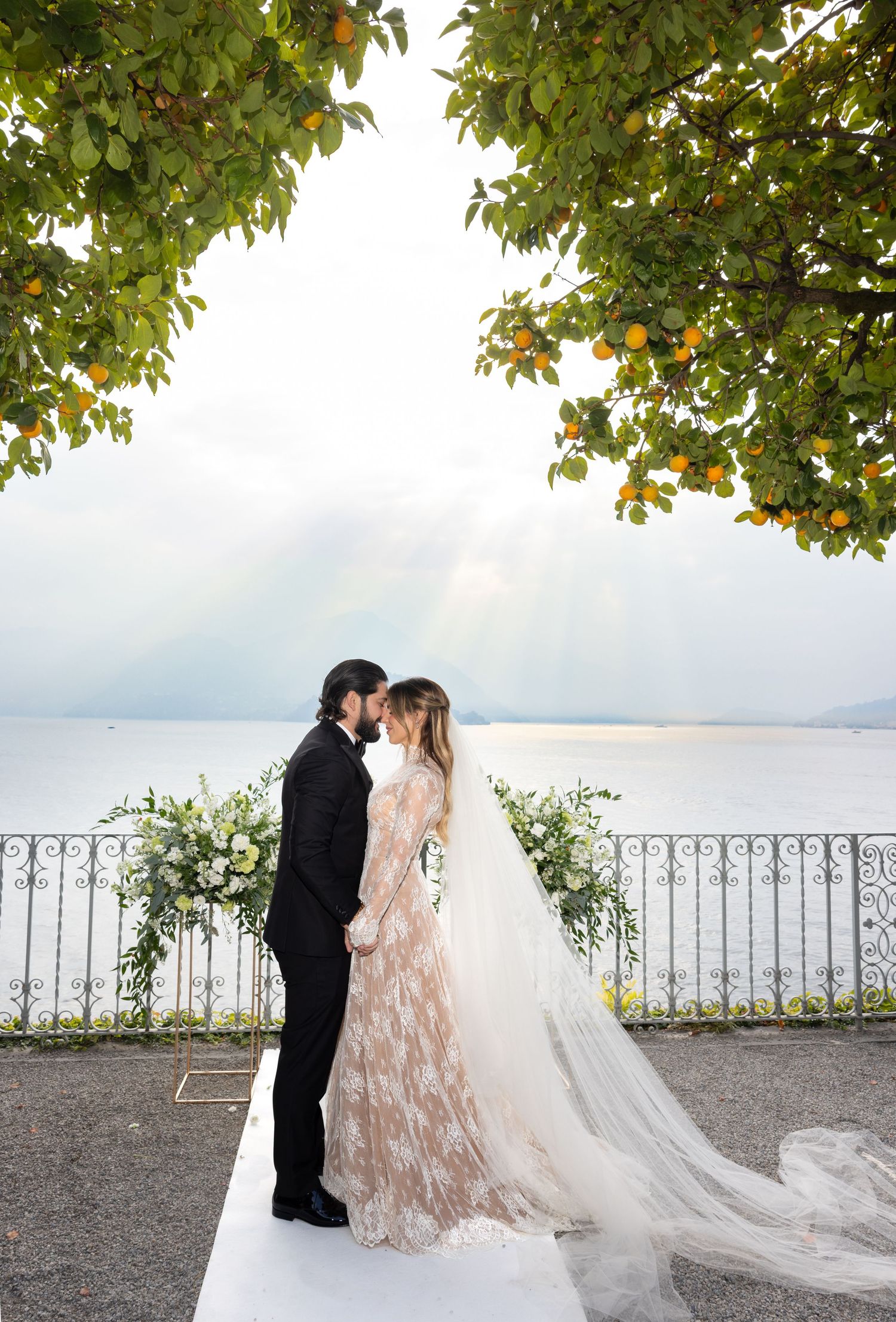 Elegant wedding couple embracing on a scenic overlook with lush trees and mountain views.