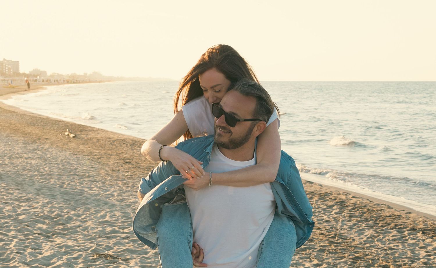 Couple sharing romantic moments on a sandy beach during golden hour sunset.