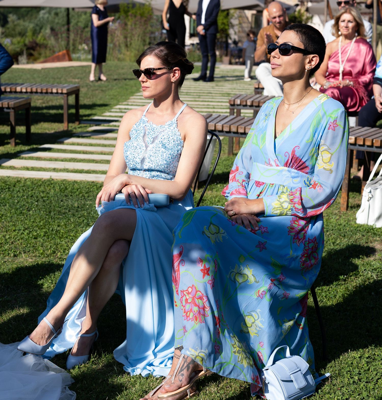 Wedding guests in colorful summer dresses relaxing on lawn chairs outdoors.