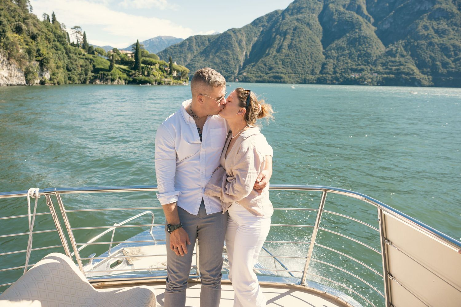 Couple enjoying romantic moment on yacht with lake and mountain backdrop.