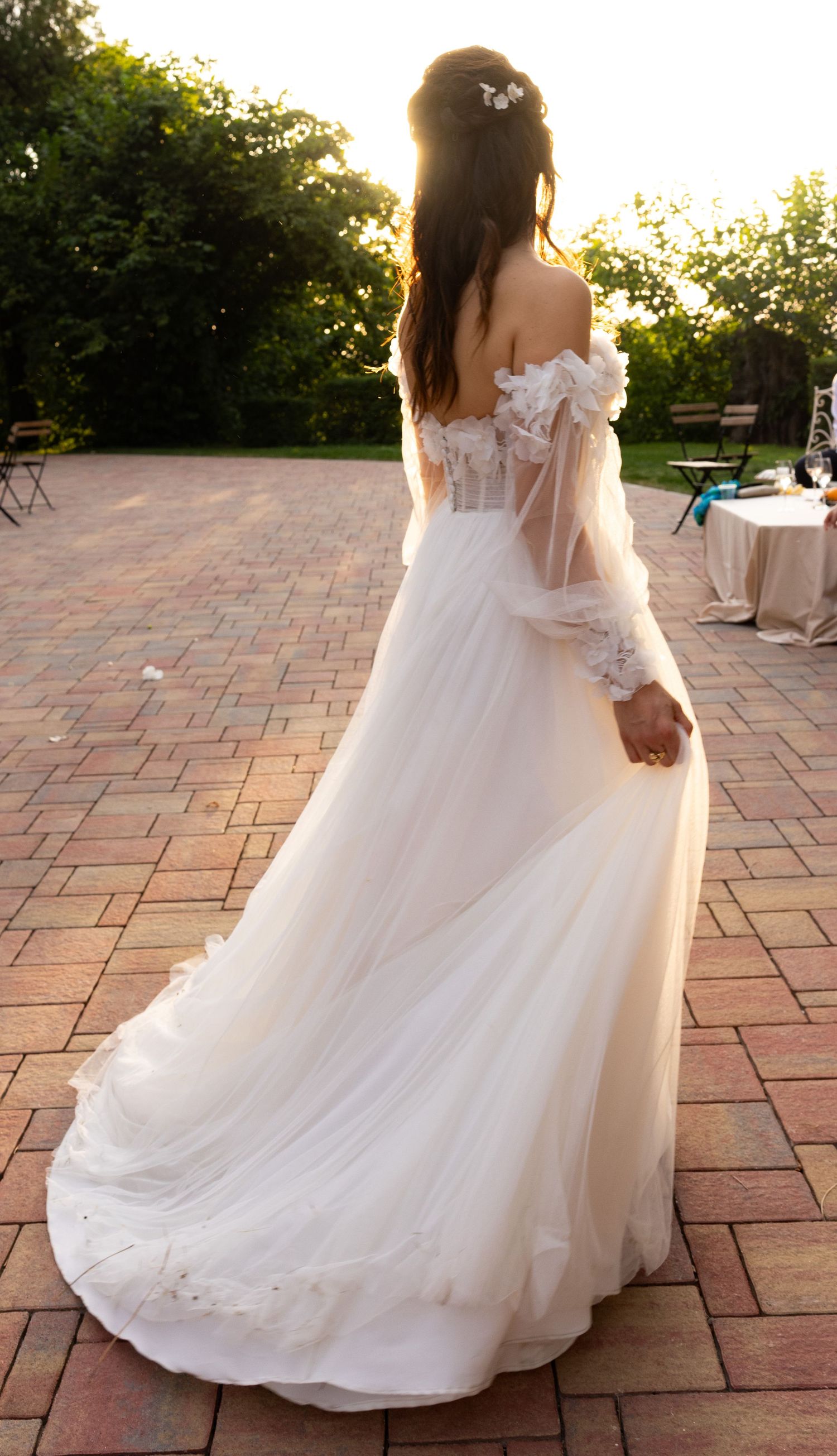 Flowing white wedding dress train trailing across brick pavers at sunset.