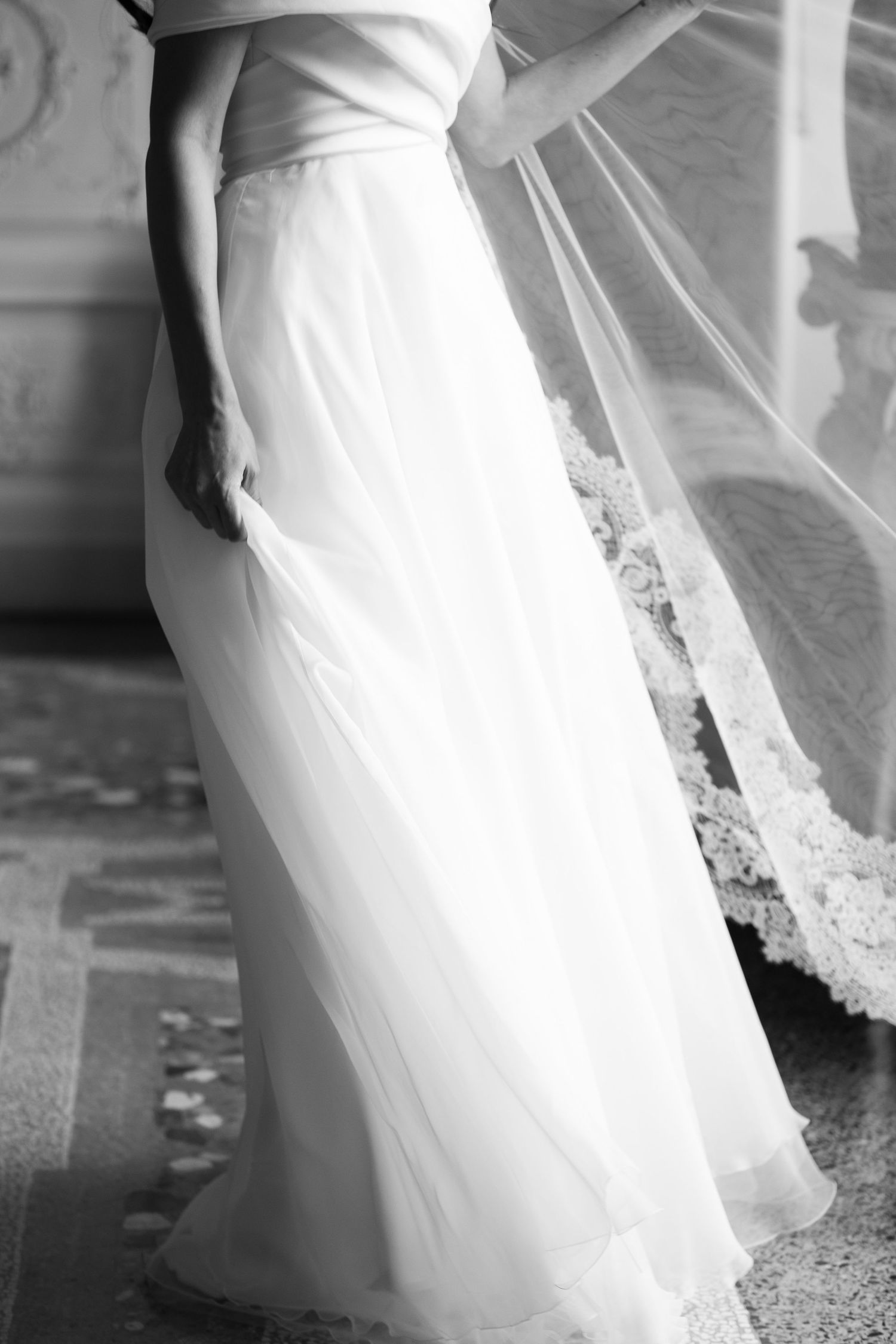 Close-up details of a flowing white wedding dress with delicate lace trim.