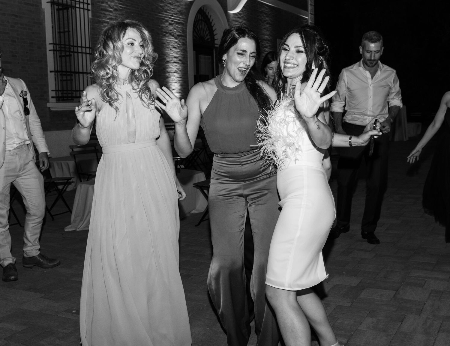 Black and white photo of guests dancing and celebrating at an outdoor wedding reception.